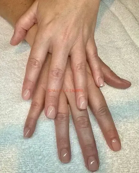 Two hands with nude-colored nail polish, resting on a white surface. Two hands with nude-colored nail polish, resting on a white surface.
