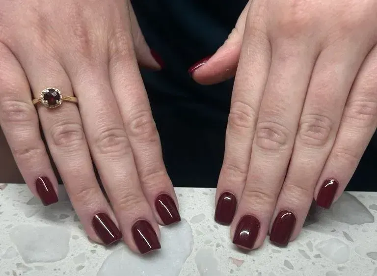 Hands with square burgundy nails, wearing a gold ring with a red gemstone. Hands with square burgundy nails, wearing a gold ring with a red gemstone.