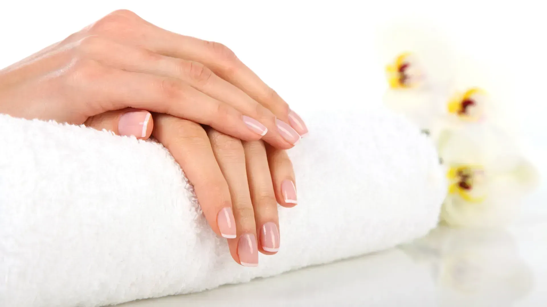 Hands with French manicure resting on a white rolled towel, with white flowers. Hands with French manicure resting on a white rolled towel, with white flowers.