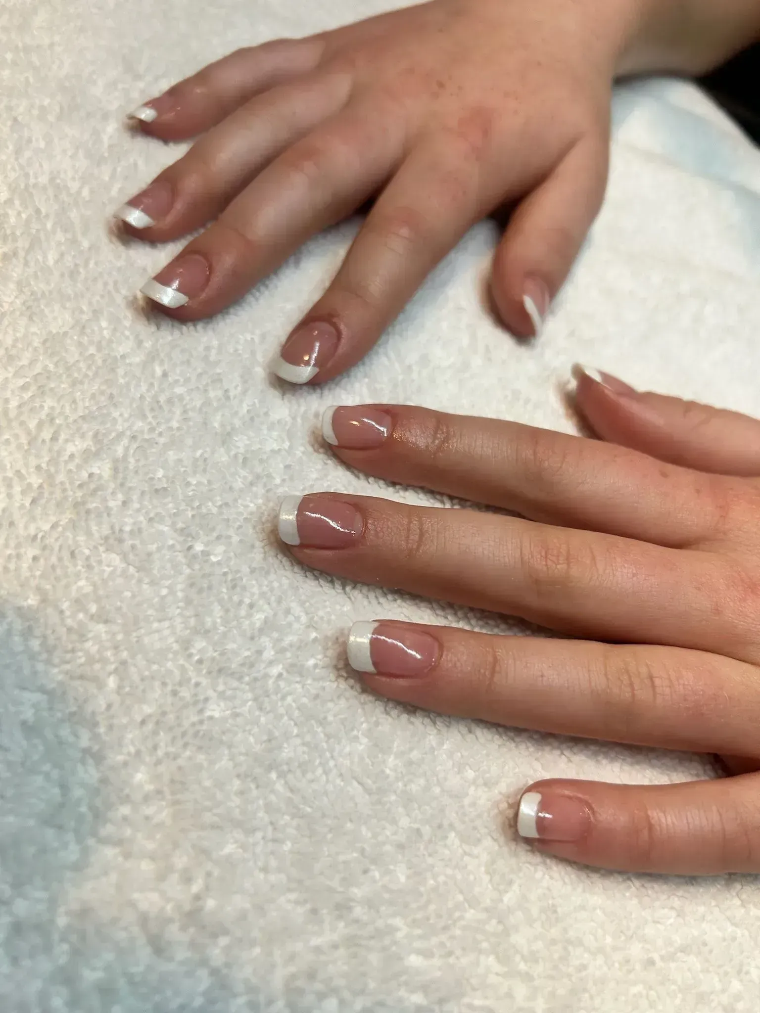 Hands with French tip manicured nails resting on a white towel. Hands with French tip manicured nails resting on a white towel.