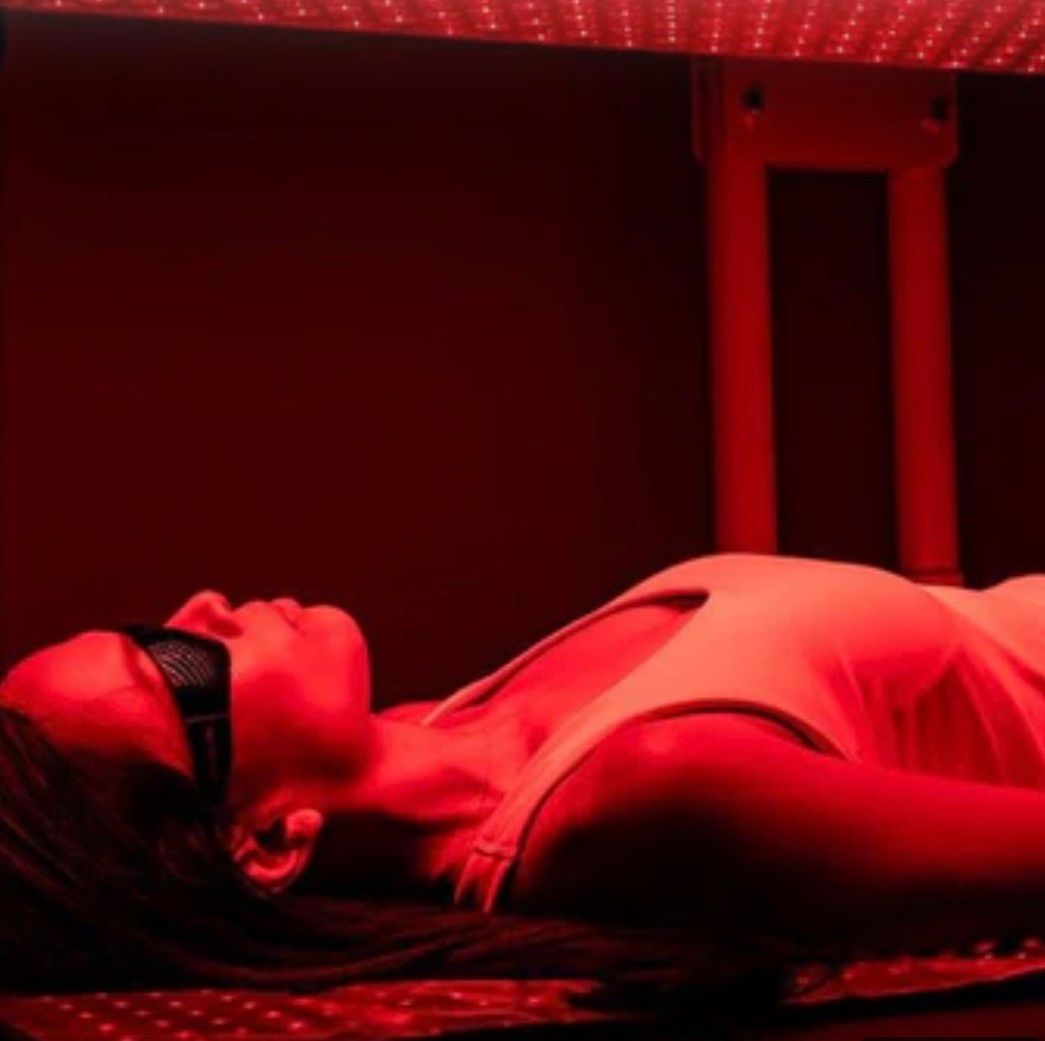 Woman lying under a full-body red light therapy panel with eye protection during a spa session