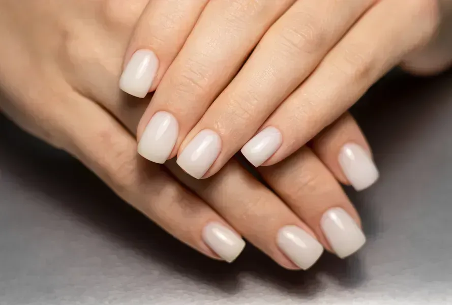 A close up of a woman's hands with white nails.