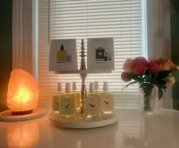 Bottles of nail polish displayed on a white table, next to a lit salt lamp and a vase of flowers. Bottles of nail polish displayed on a white table, next to a lit salt lamp and a vase of flowers.