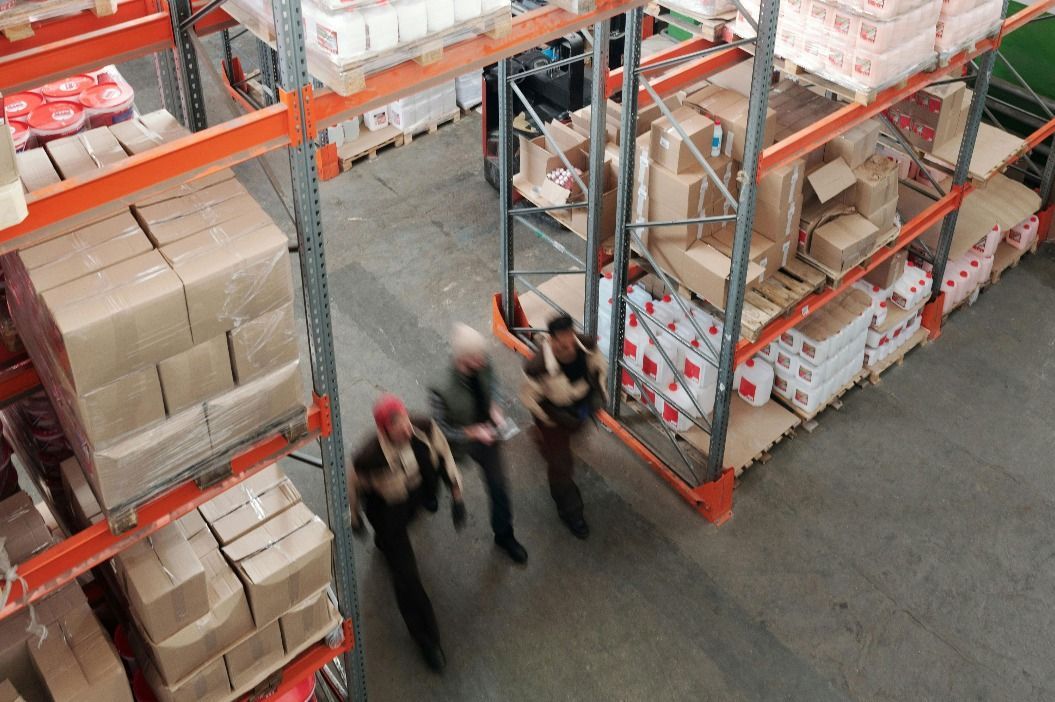 Trois personnes traversent l'allée d'un entrepôt rempli de hautes étagères de cartons.