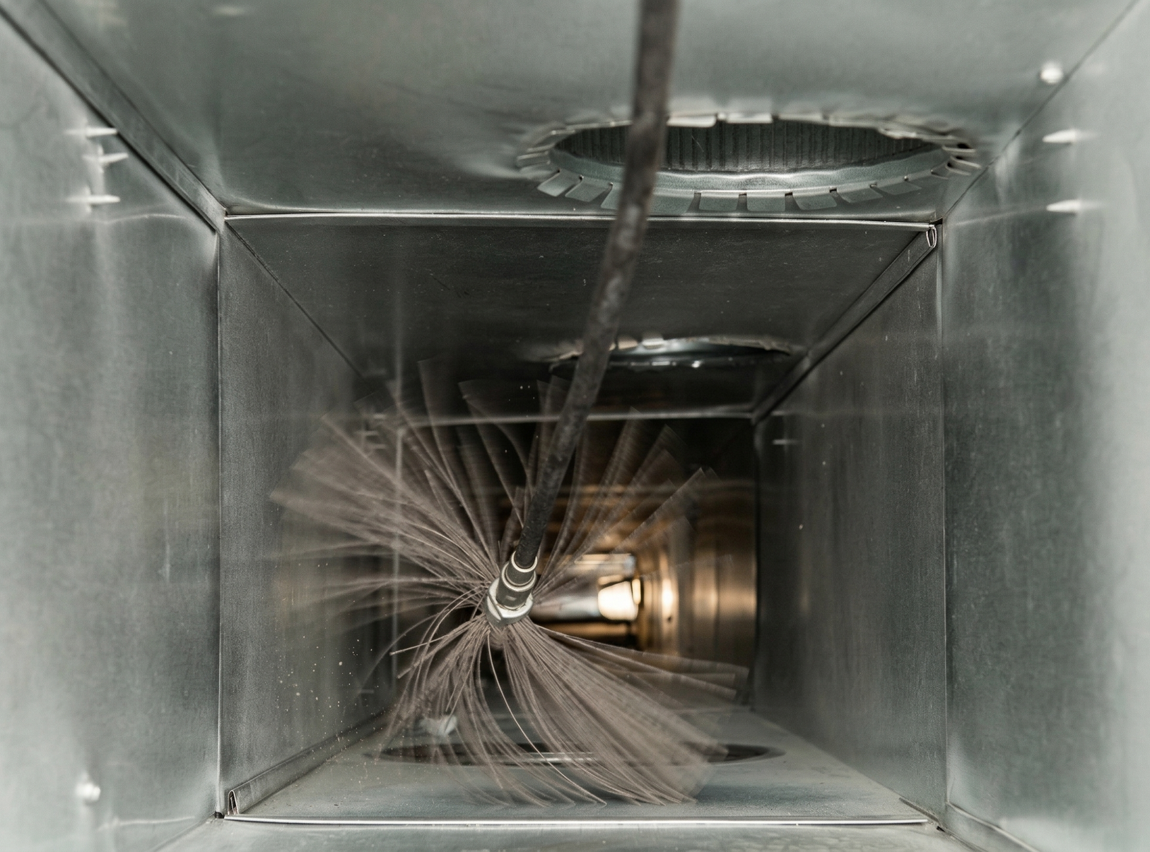 Une brosse rotative nettoie l'intérieur d'un conduit d'air rectangulaire en métal d'un système de chauffage.