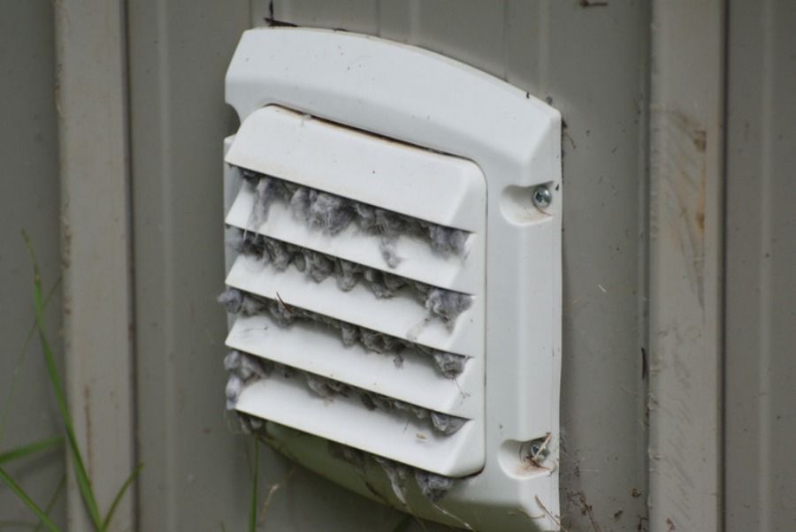 Un employé utilise un embout d'aspirateur fixé à une longue perche pour nettoyer une grille d'aération au plafond.