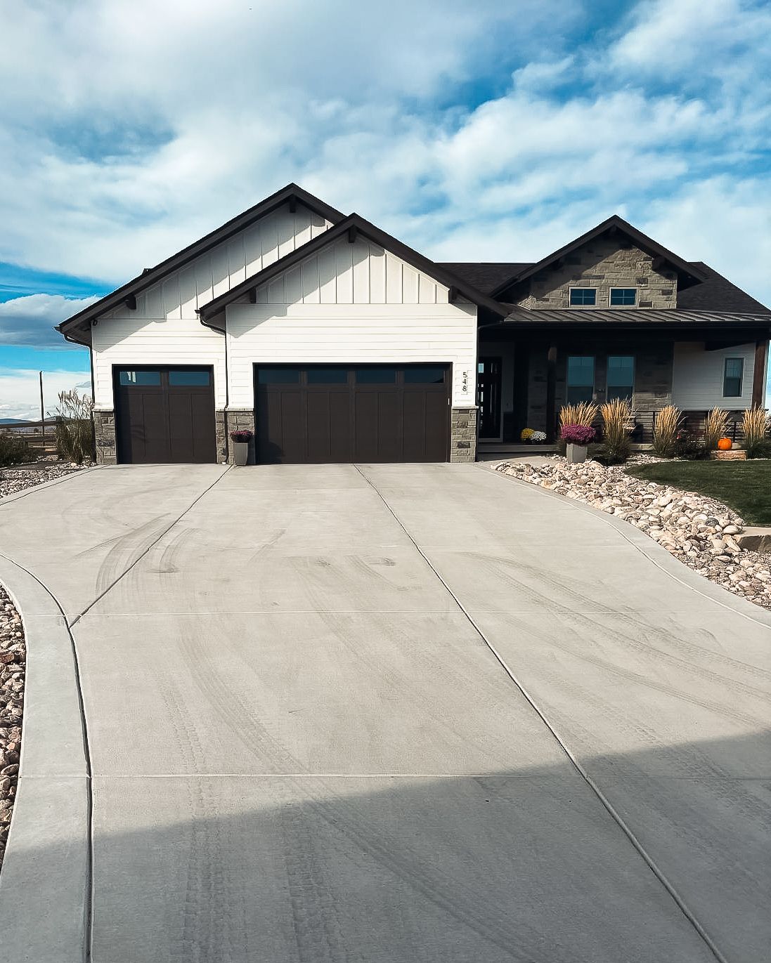 A large white house with two garage doors and a concrete driveway leading to it.