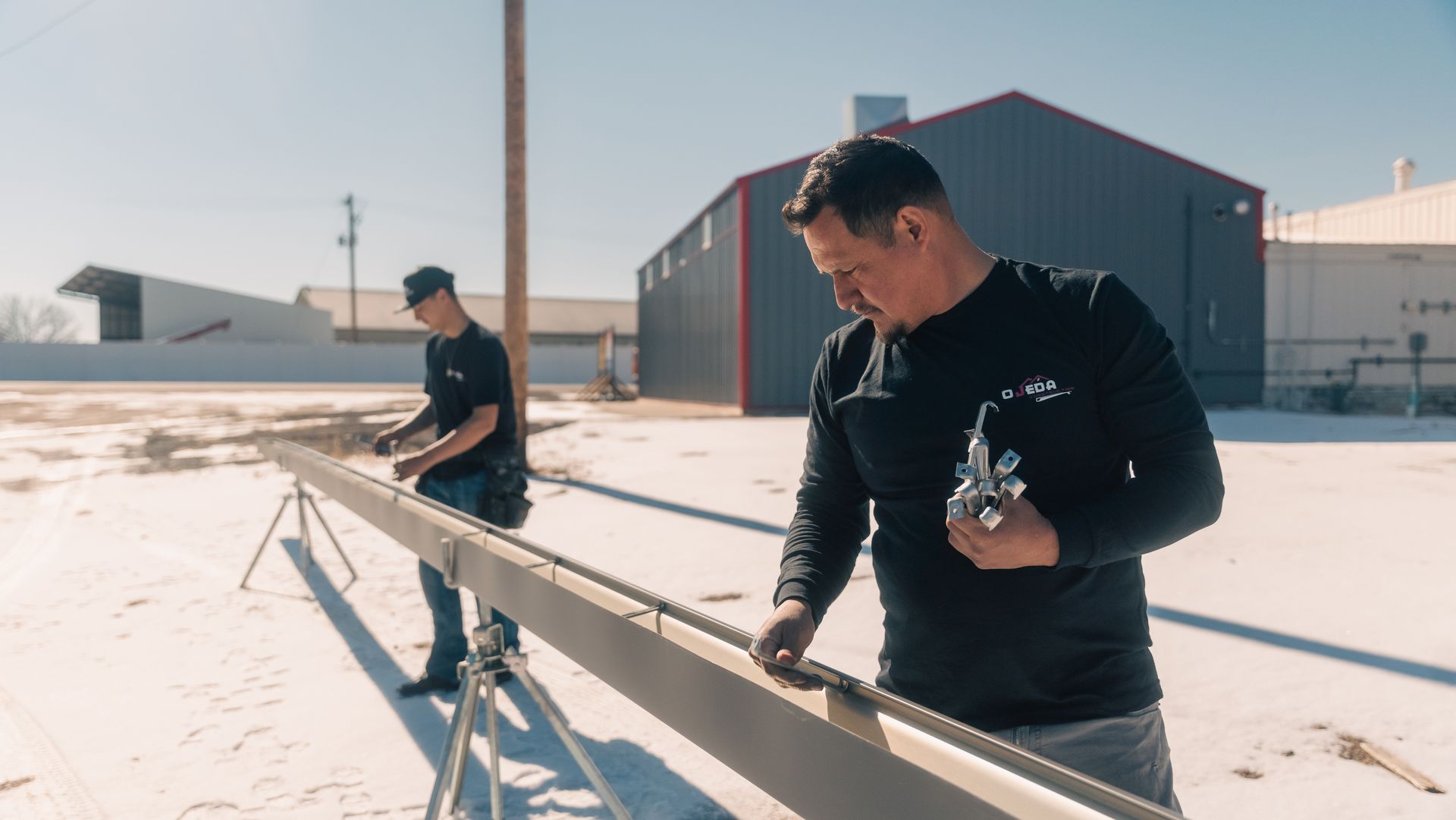 Two men are working on a piece of gutter in the snow.