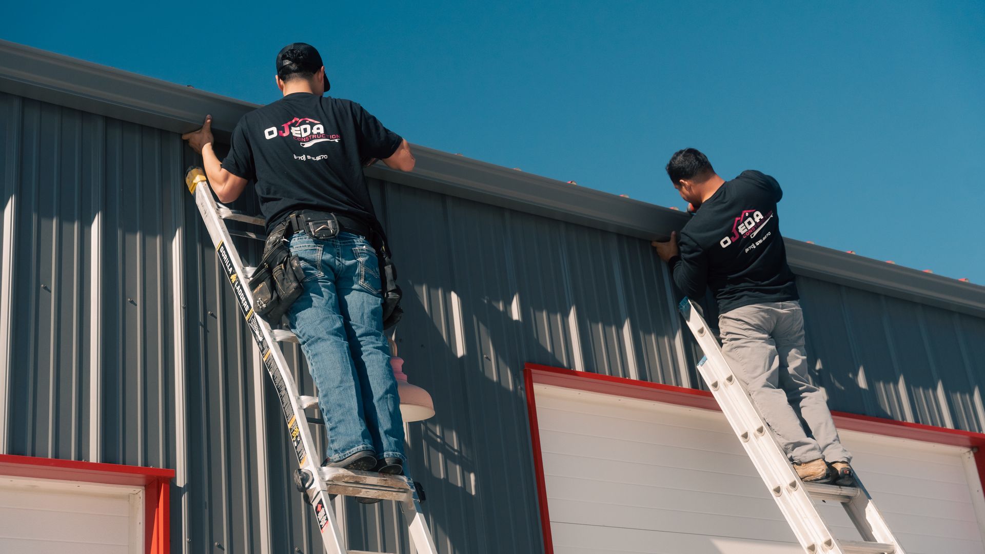 Two men are standing on ladders working on the side of a building.