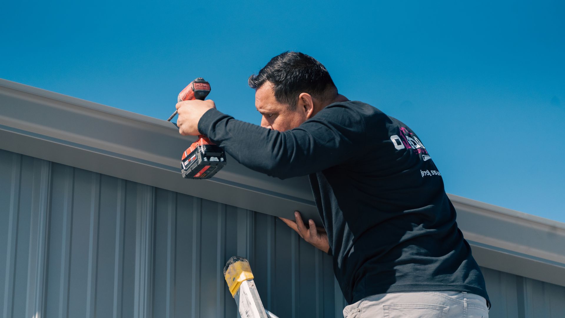A man is working on the roof of a building with a drill.