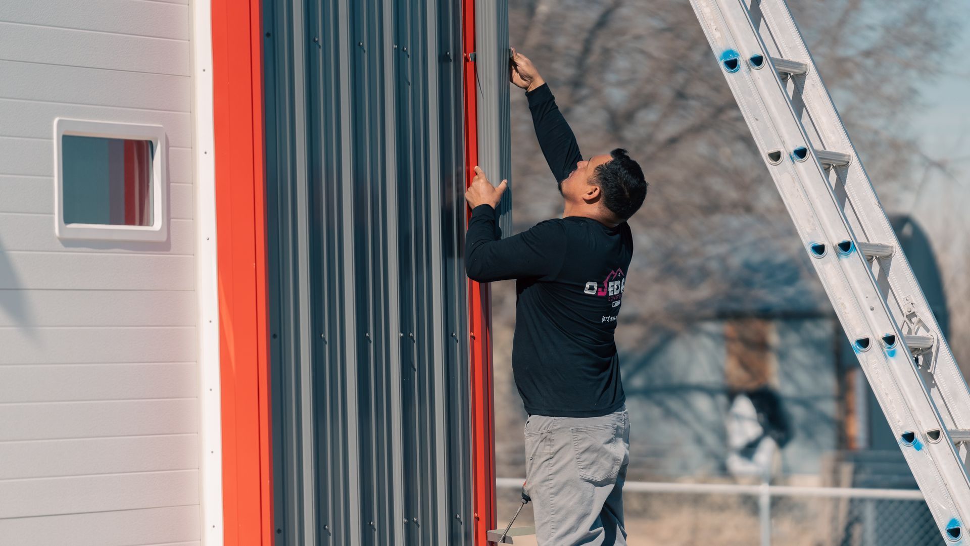 A man is standing on a ladder installing gutters.