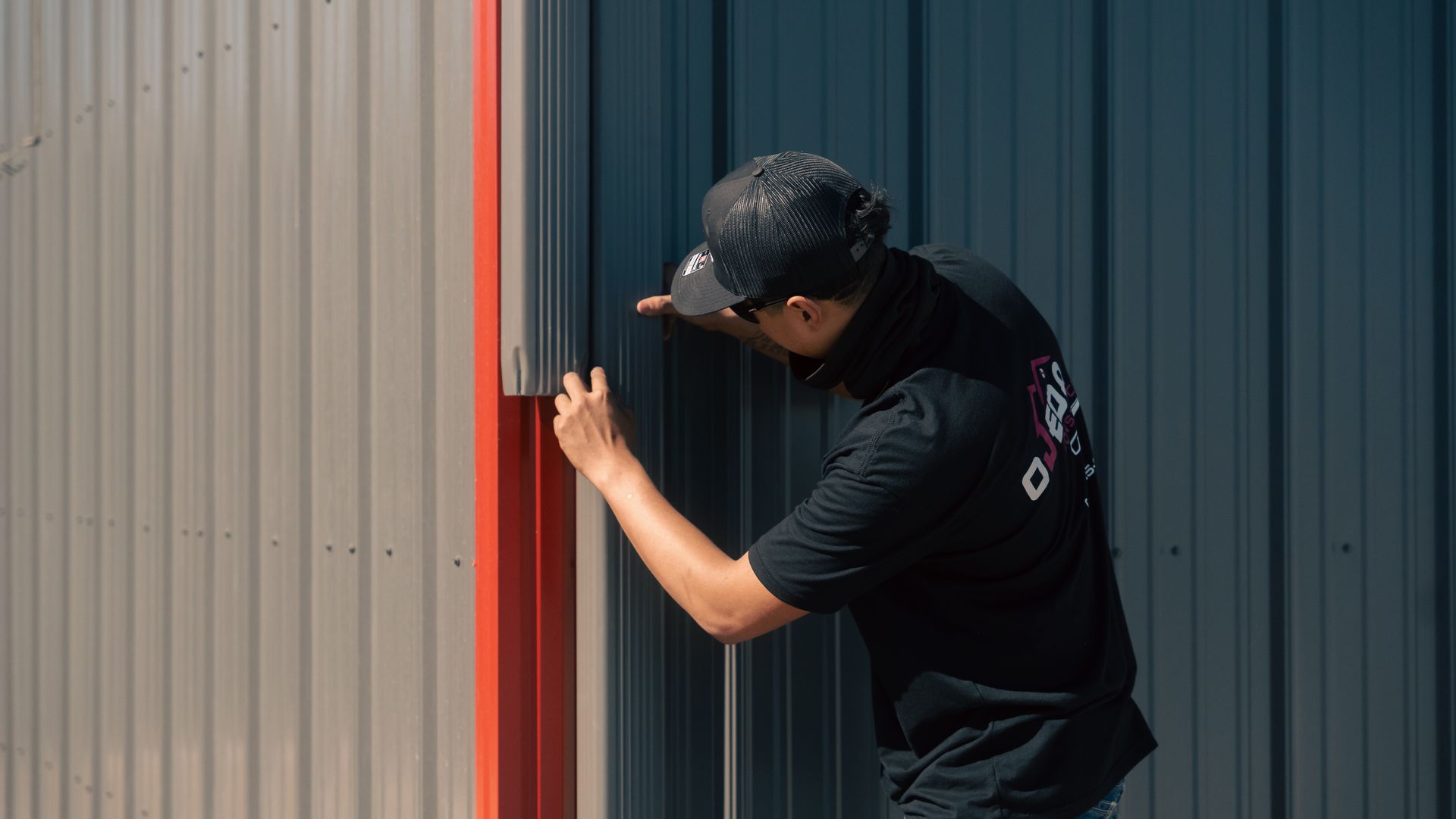 A man is installing gutters on a metal building with a red trim.
