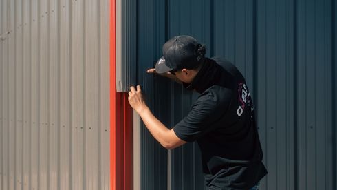 A man is installing gutters on a metal building with a red trim.