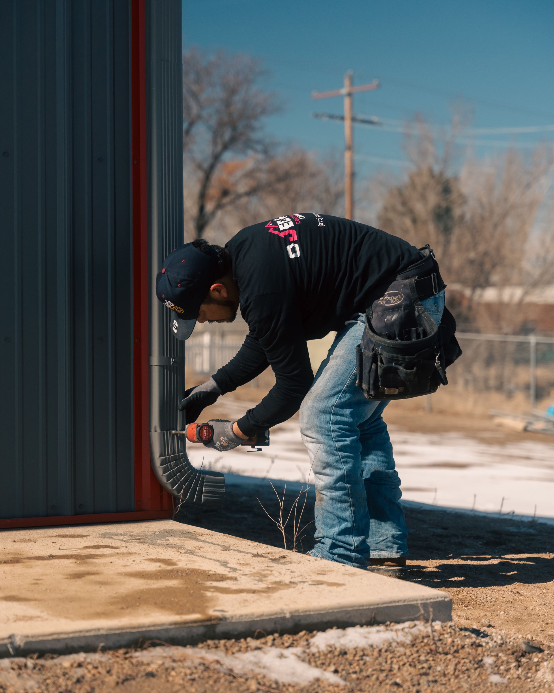 A man is installing a drain pipe on the side of a building.