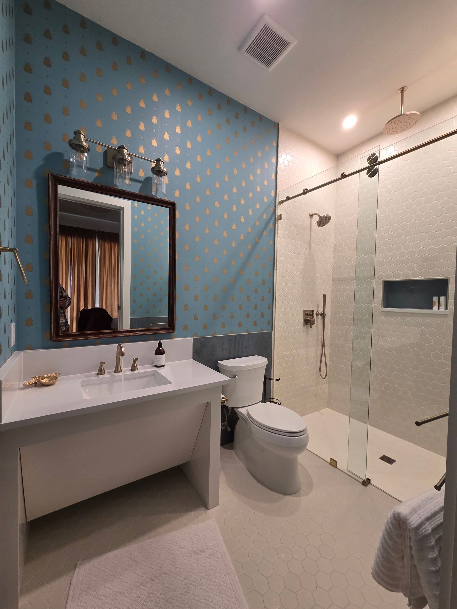 Modern bathroom with blue accent wall, vanity, toilet, glass shower, and mirror lights