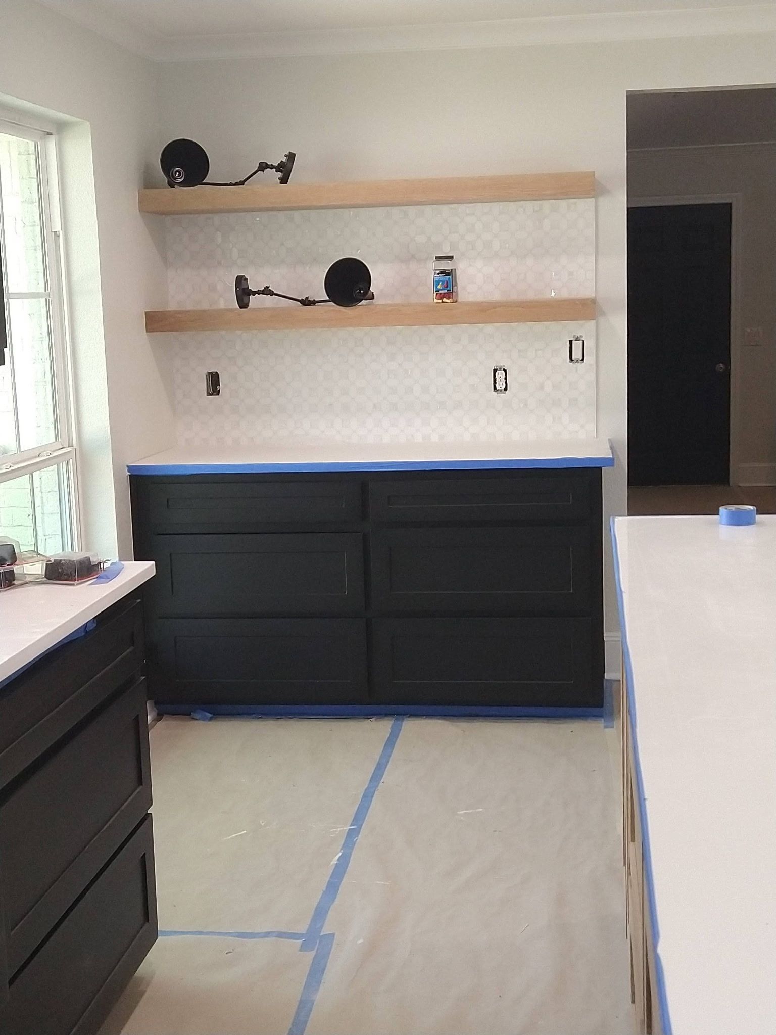 Kitchen under renovation with black cabinets, light wood shelves, and blue tape marking the floor area