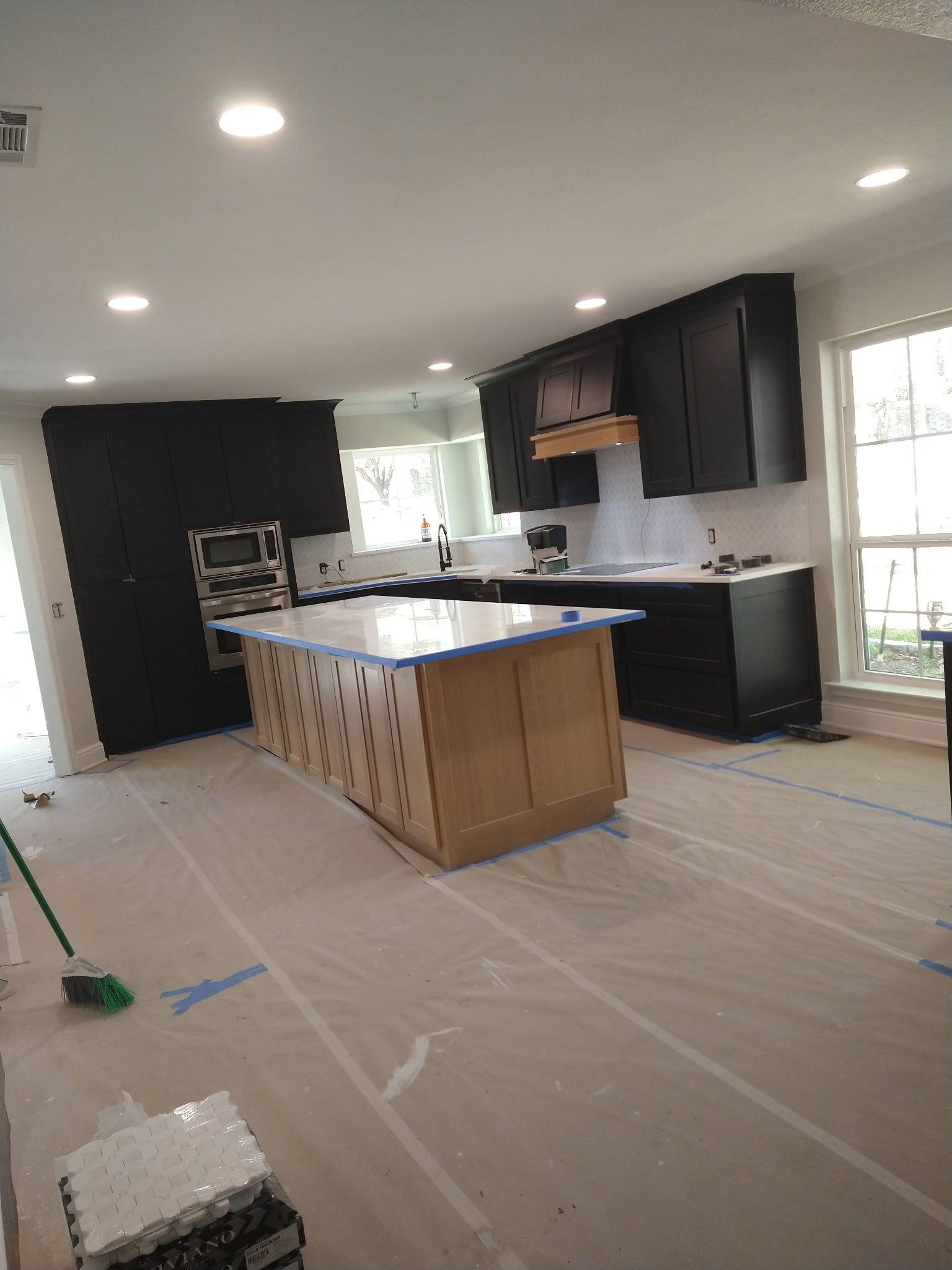 Unfinished kitchen with dark cabinets, an island, white walls, and protective floor covering during renovation