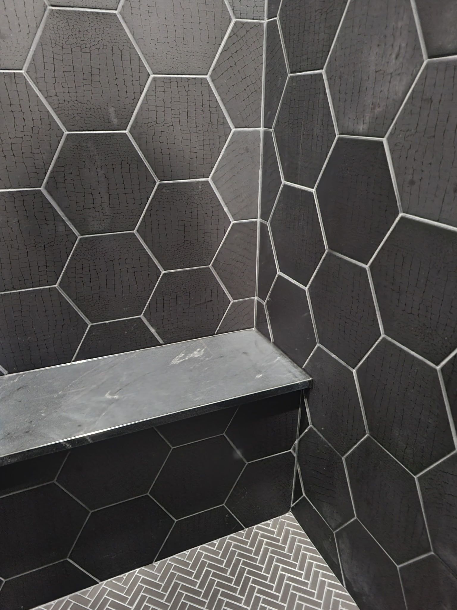 Dark hexagonal tiled shower corner with a built-in shelf and patterned floor drain mat