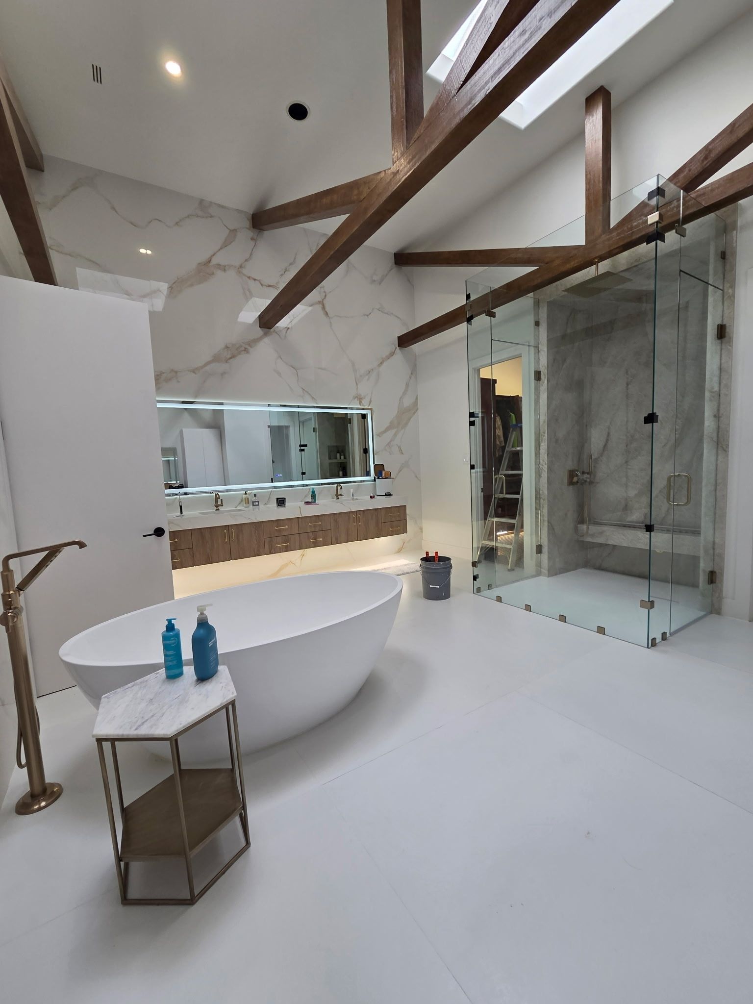 Modern bathroom with freestanding tub, glass shower, and exposed wooden beams, in white and gray tones