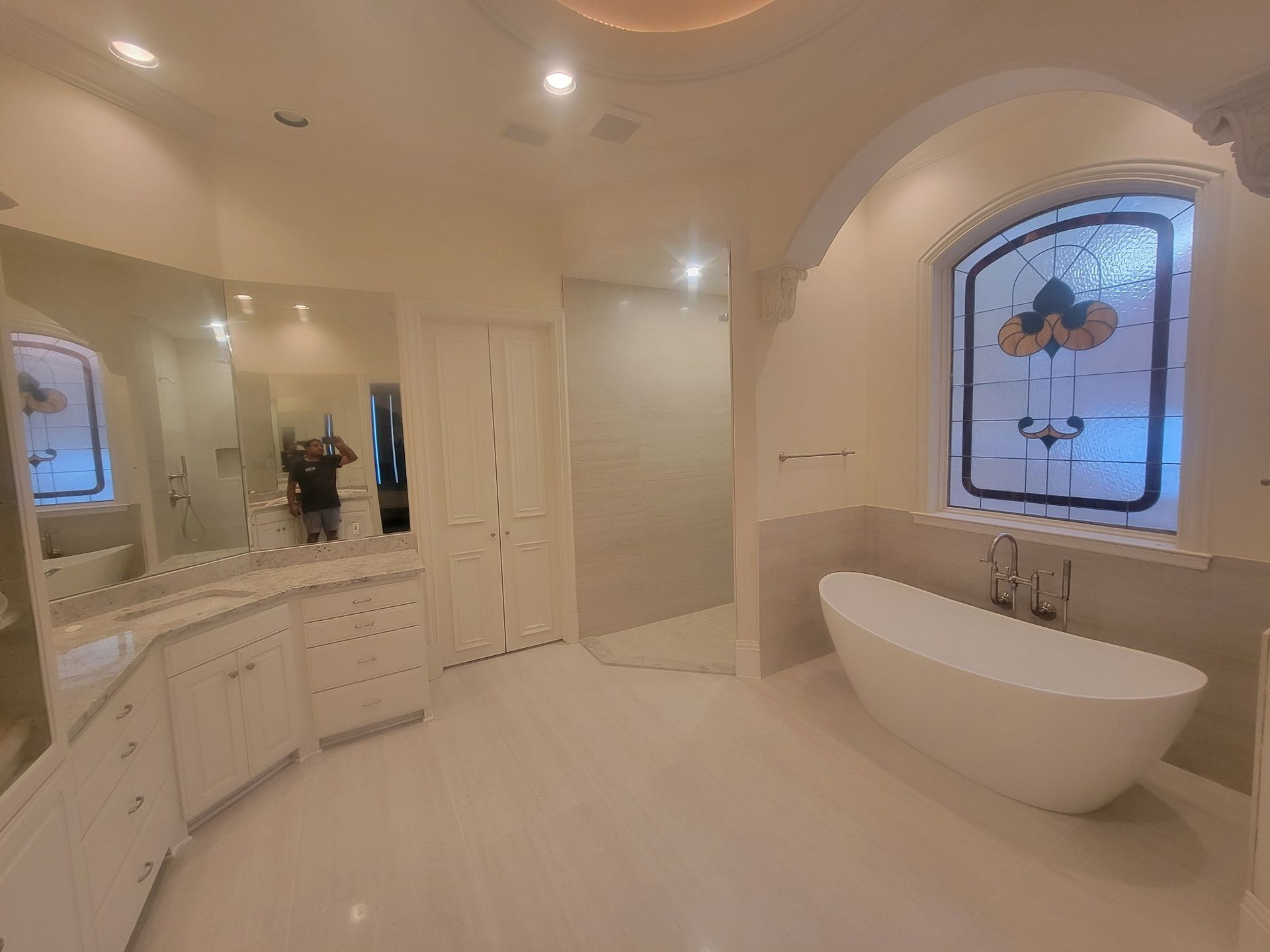 Elegant cream bathroom with vanity, mirror, skylight, and a freestanding tub by stained glass window