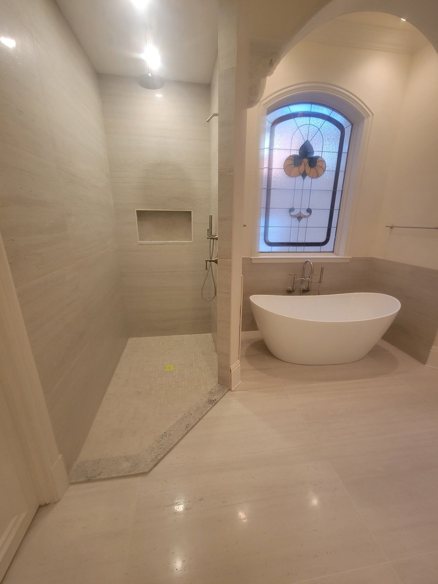 Elegant beige bathroom with a walk-in shower, freestanding tub, and stained-glass window.