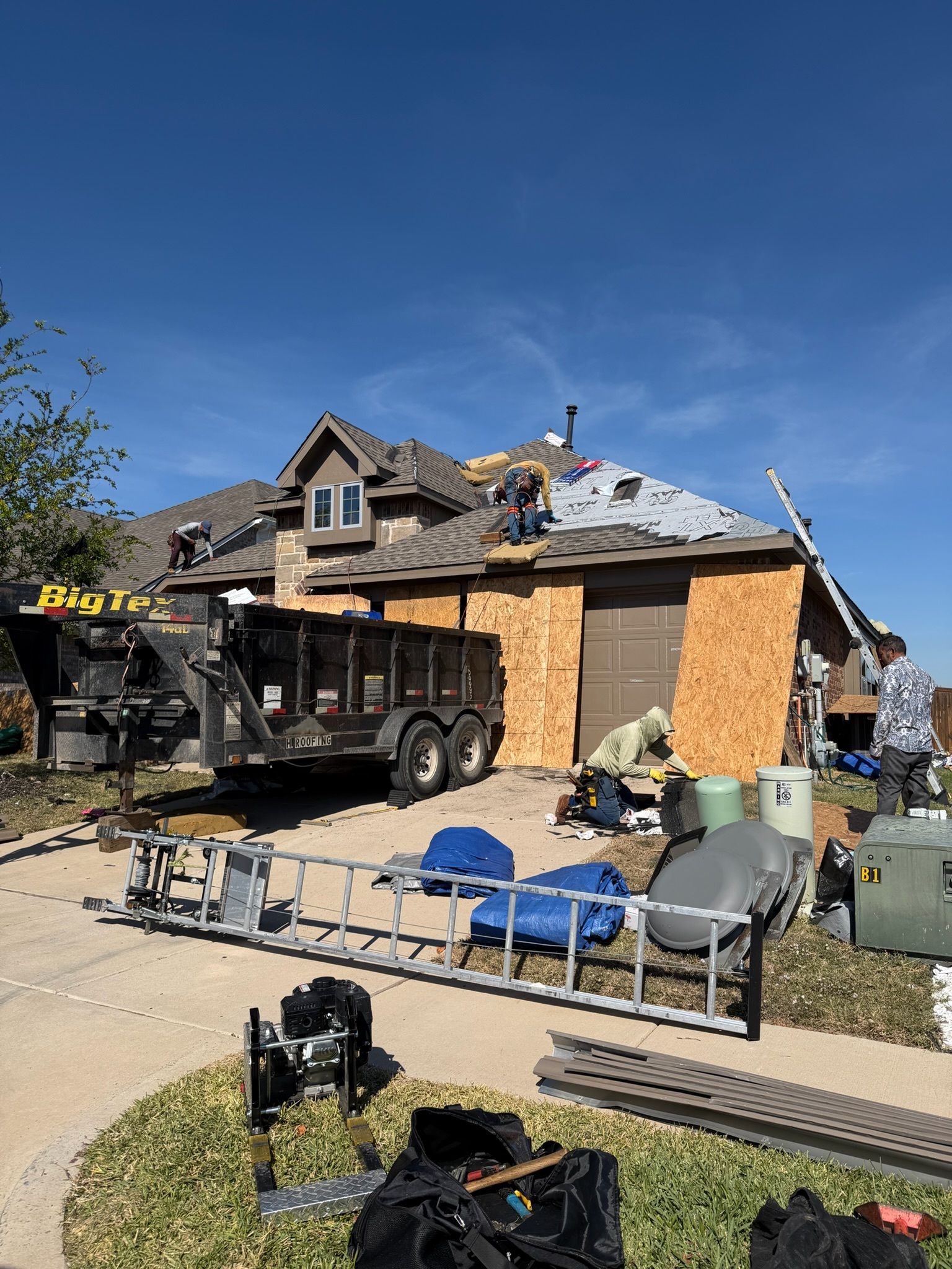 Damaged house with roof torn off, boarded windows, and construction equipment in the driveway.