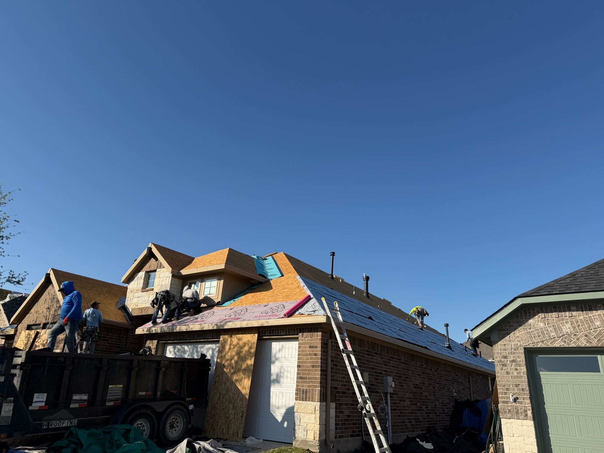 Partially built house with workers, roof framing, and a ladder under a clear blue sky