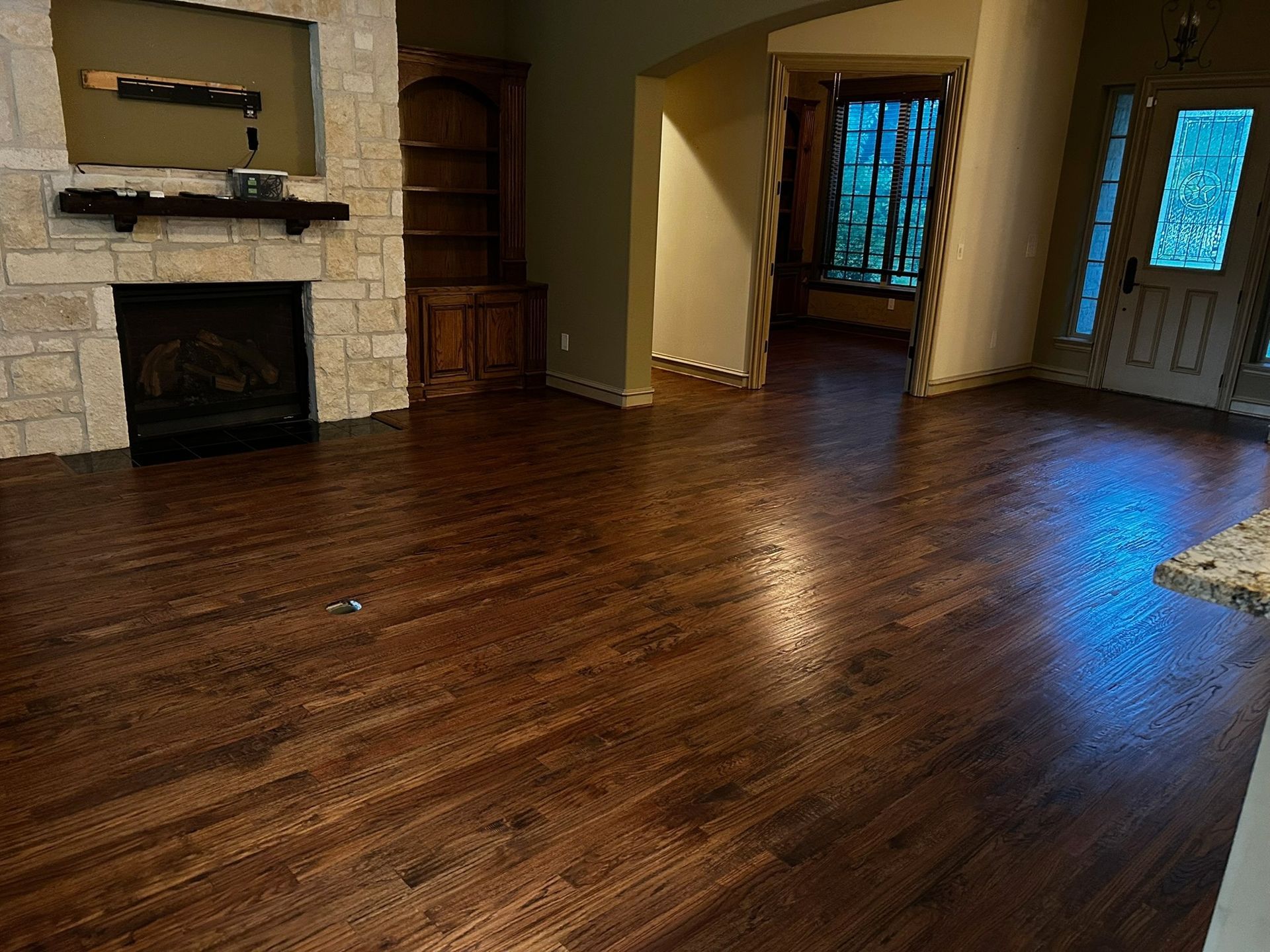 Spacious living room with hardwood floors, stone fireplace, and open doorway to a hallway and front door.