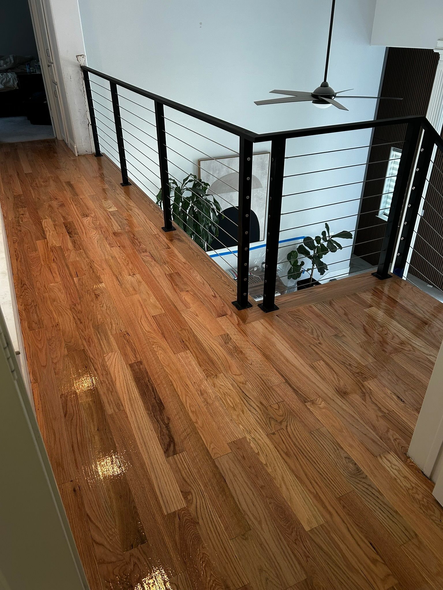 Indoor hallway with wood floors, black cable railing, and a ceiling fan overlooking a lower level.