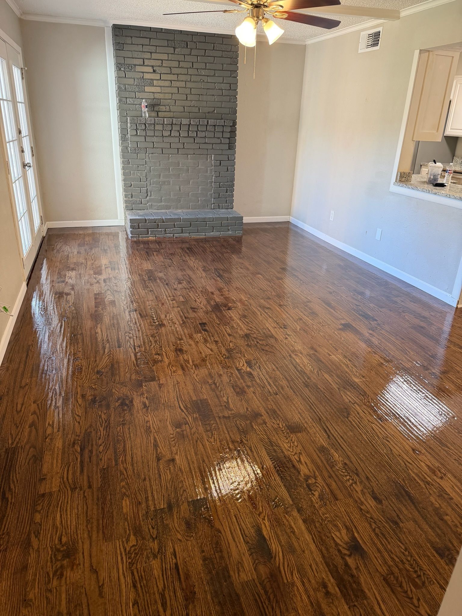 Empty living room with glossy wood floor, gray brick fireplace, and beige walls