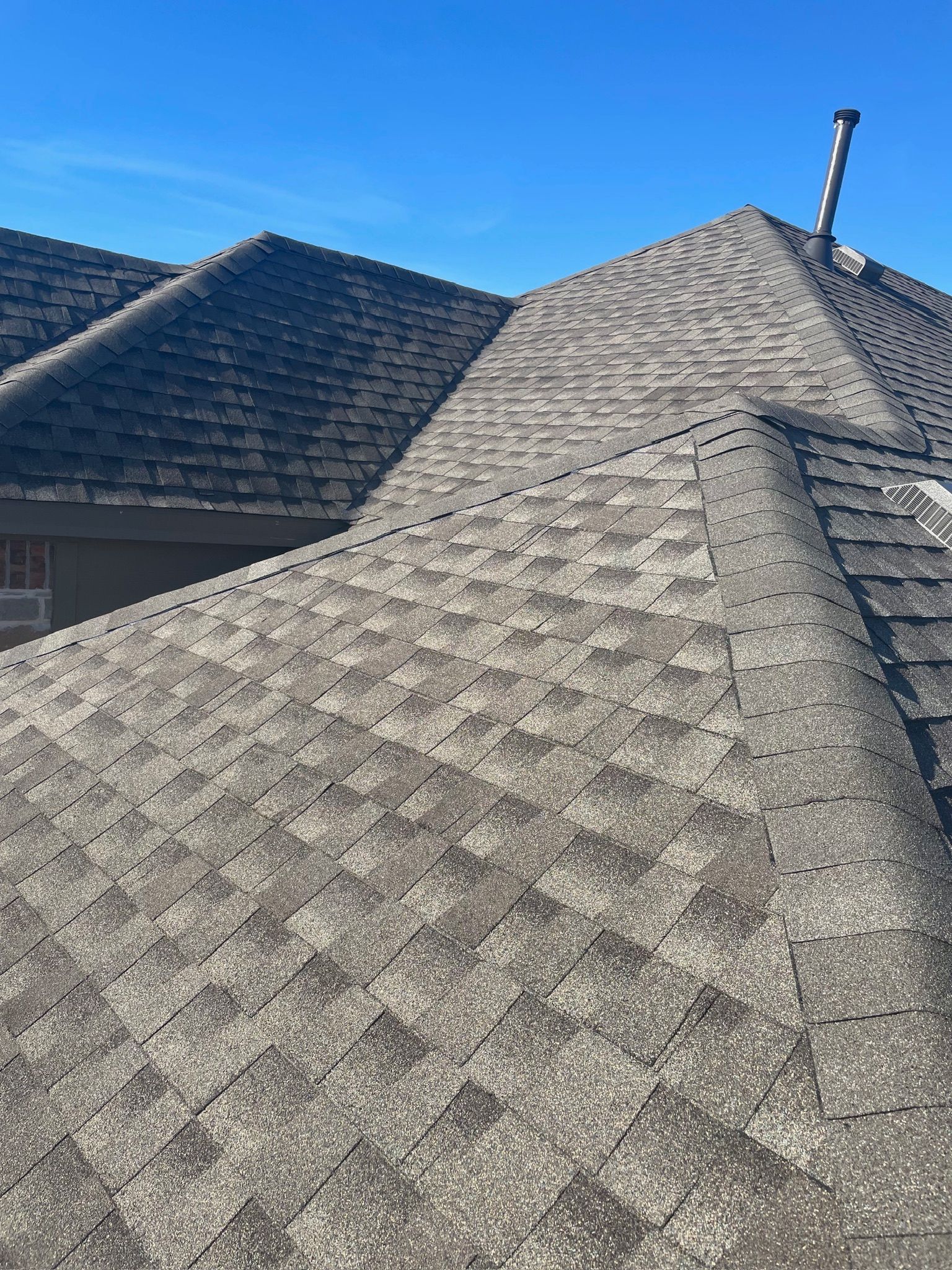 Close-up of a gray shingled roof with another roof in the background under a clear blue sky