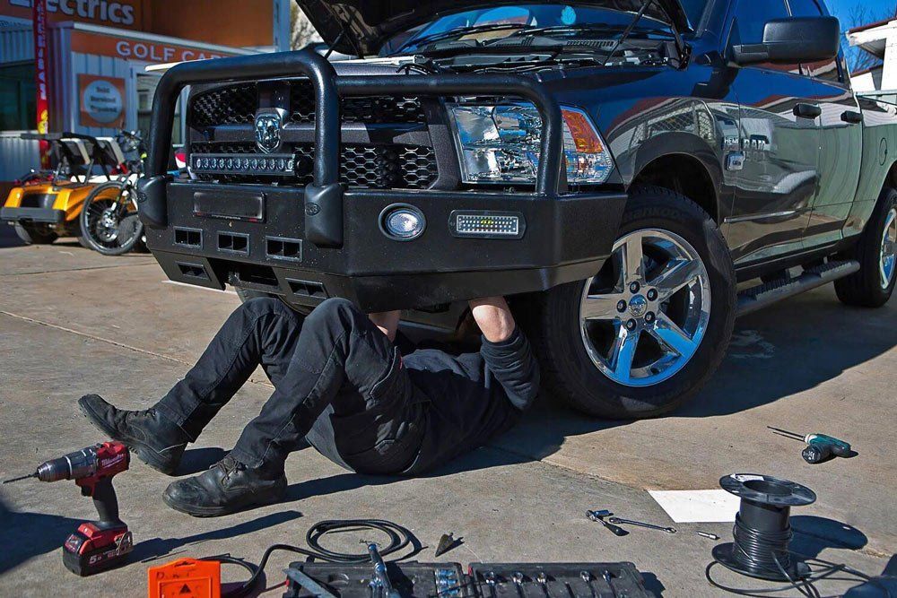 A Person Working on a Black Truck Under Its Front Bumper — Orange Auto Electrics in Orange, NSW