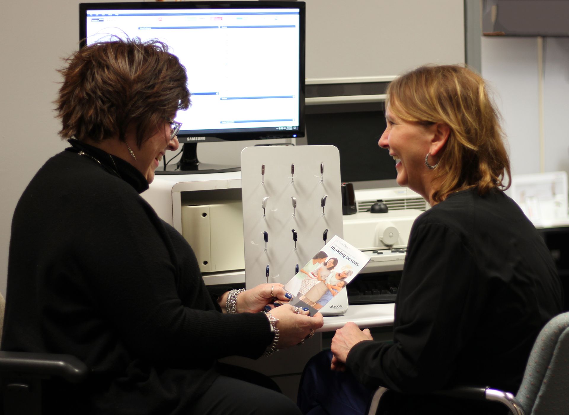 Two women are sitting at a desk and one is holding a pamphlet