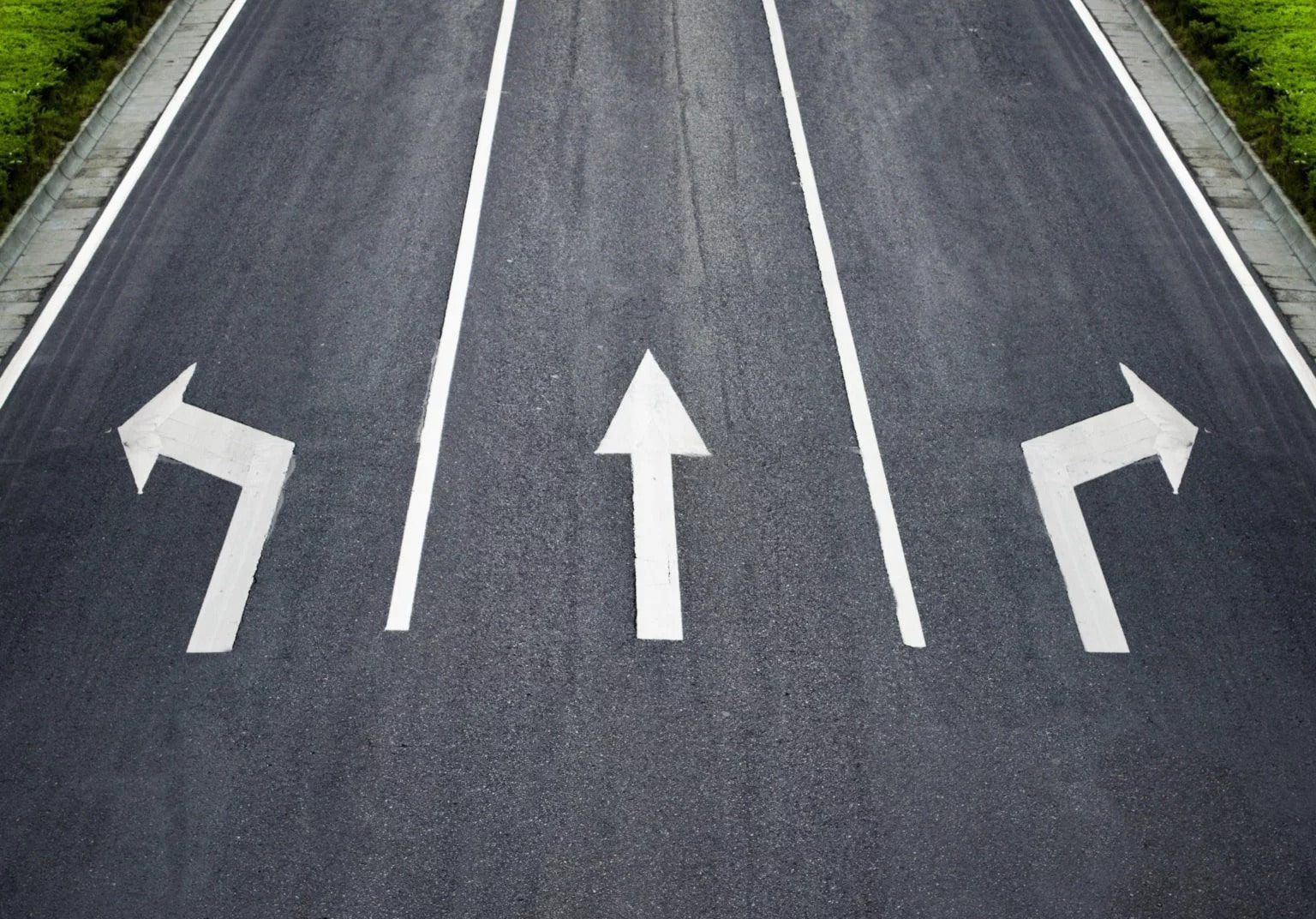 Asphalt road with three lanes and white arrows indicating left, straight, and right directions.