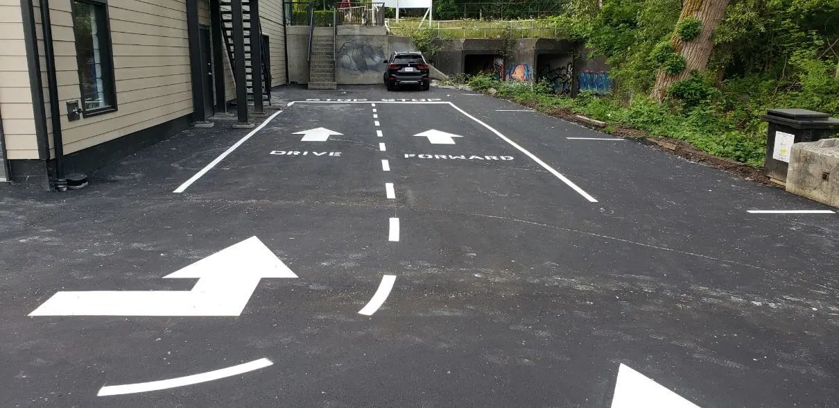 Black asphalt driveway with white arrows indicating entrance and exit, with a car at the end.