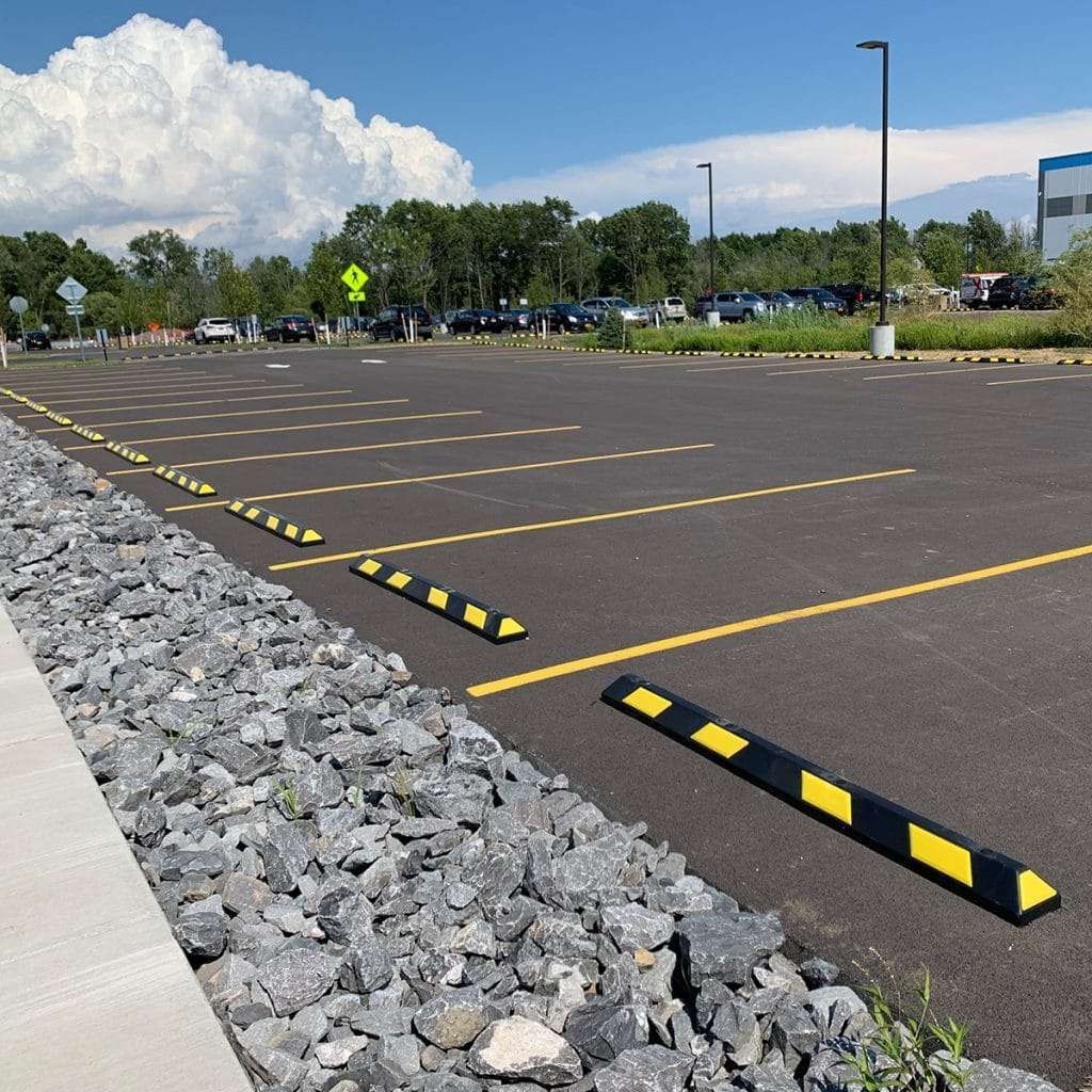 Parking lot with yellow-lined spaces, parking bumpers, and parked cars on a sunny day.