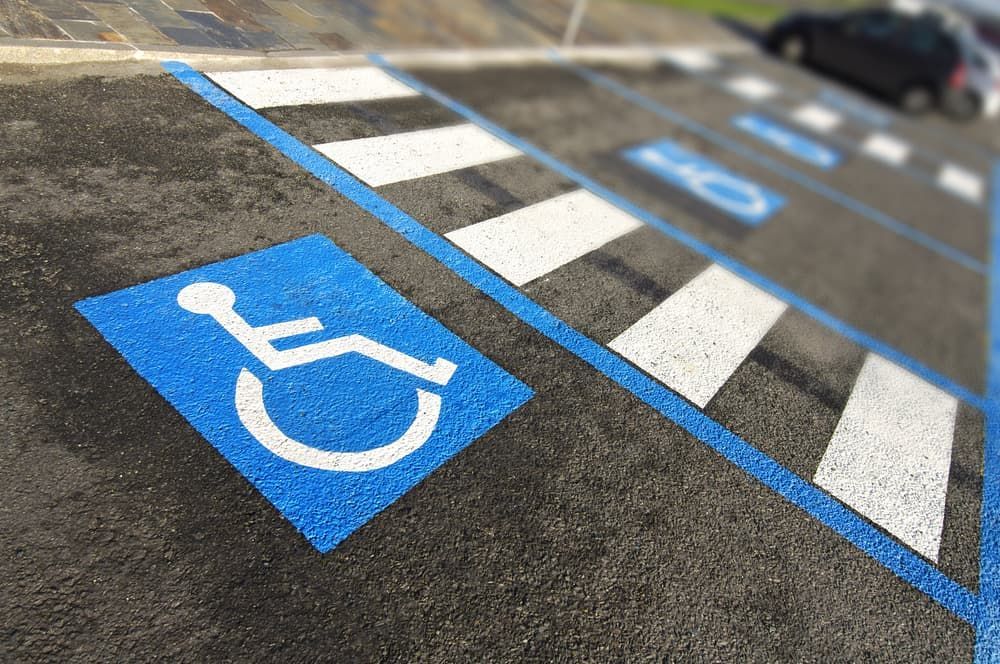 Blue and white wheelchair symbol painted on asphalt in a parking spot, with crosshatched lines and other handicap symbols.