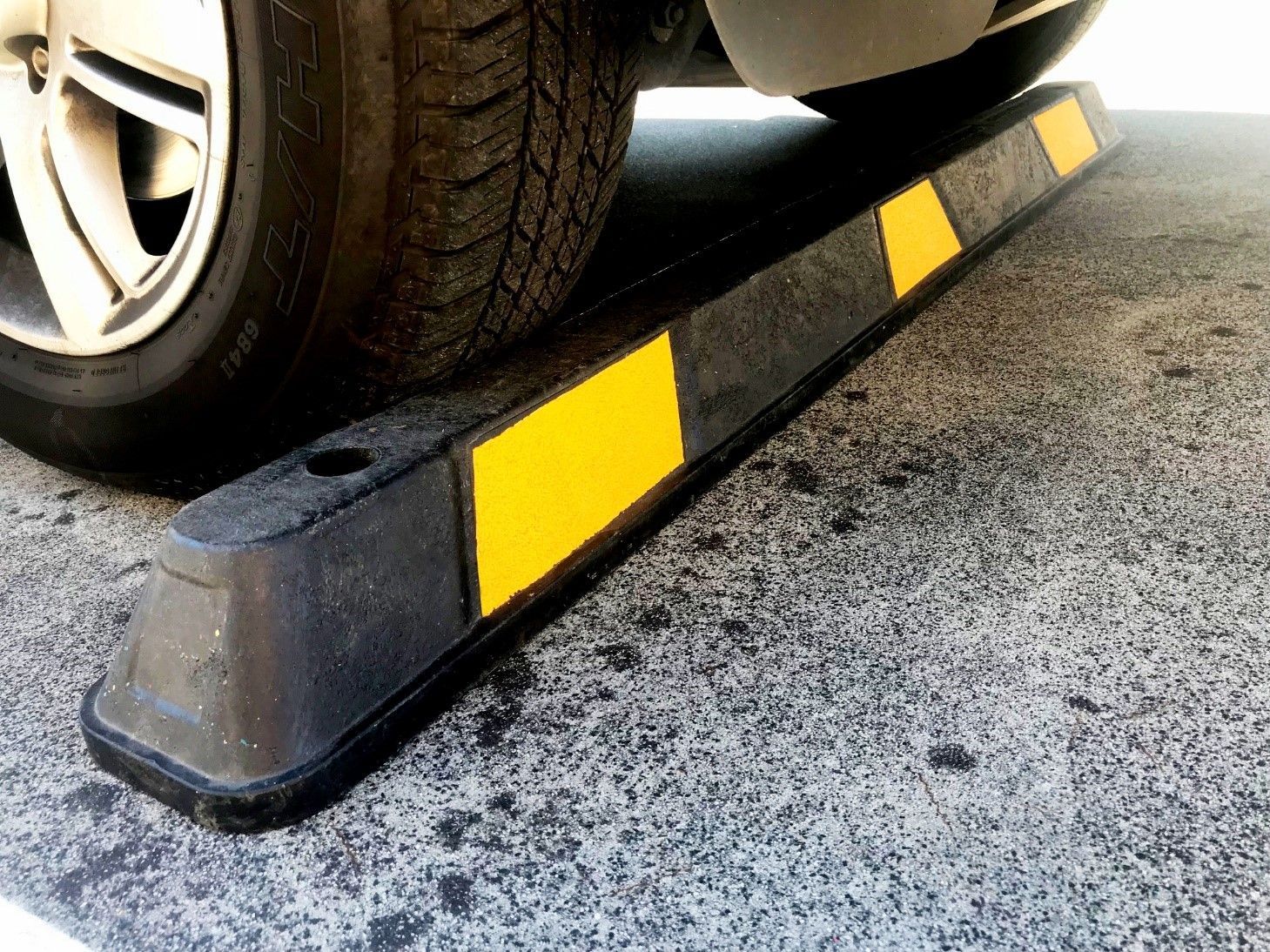 Black parking stop with yellow reflective stripes under a car tire on concrete.