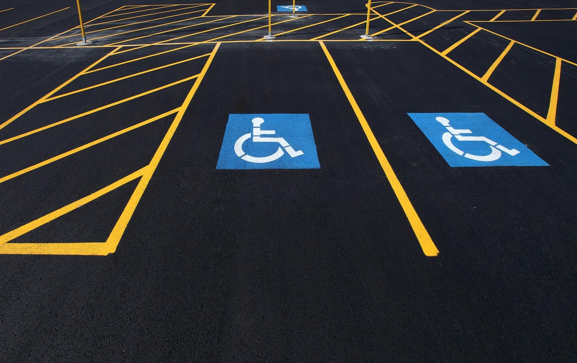 Two blue handicap parking spaces with white wheelchair symbols, marked with yellow lines on black asphalt.
