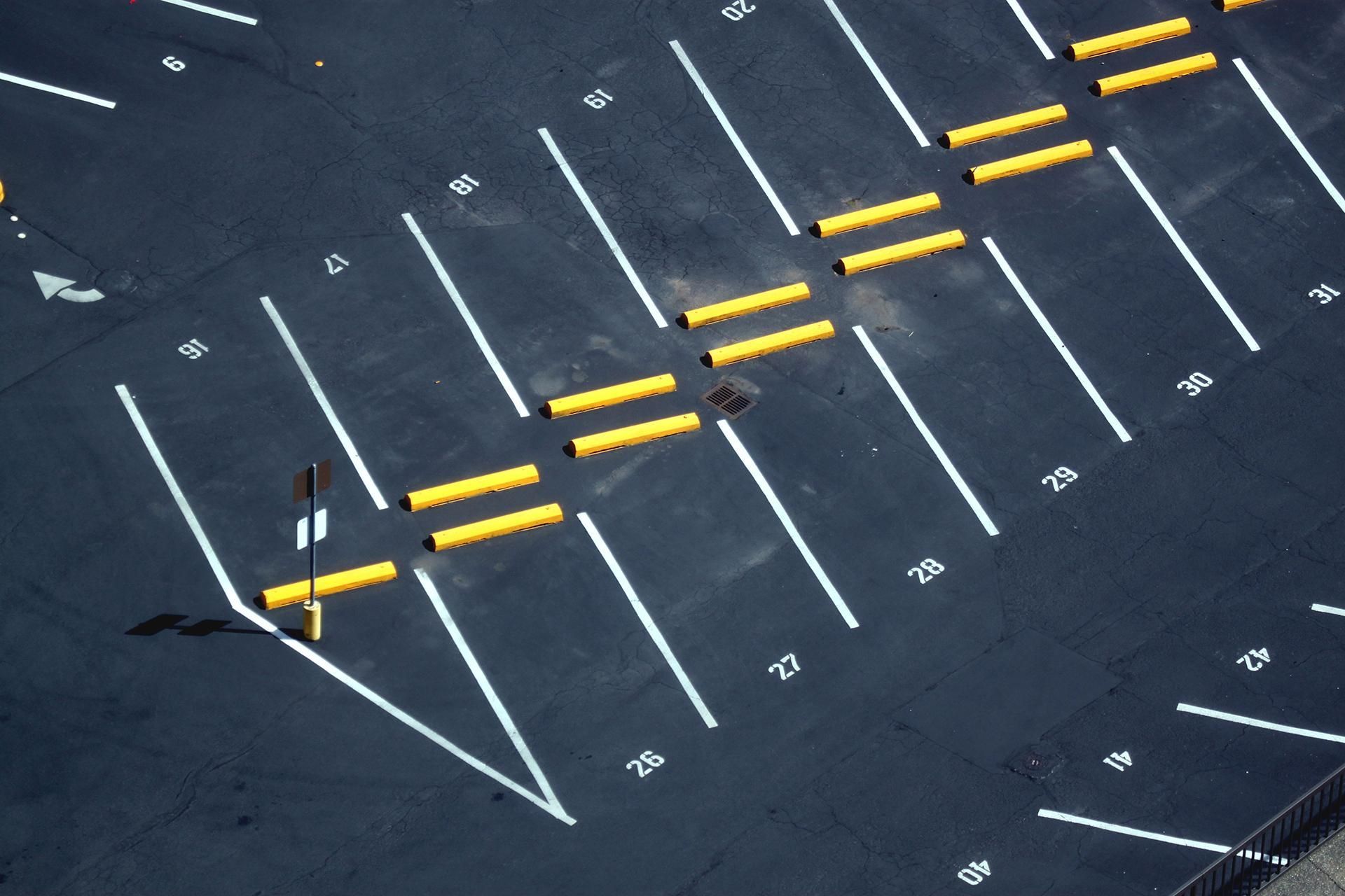 Aerial view of a parking lot with white lines, yellow parking blocks, and numerical markings on asphalt.