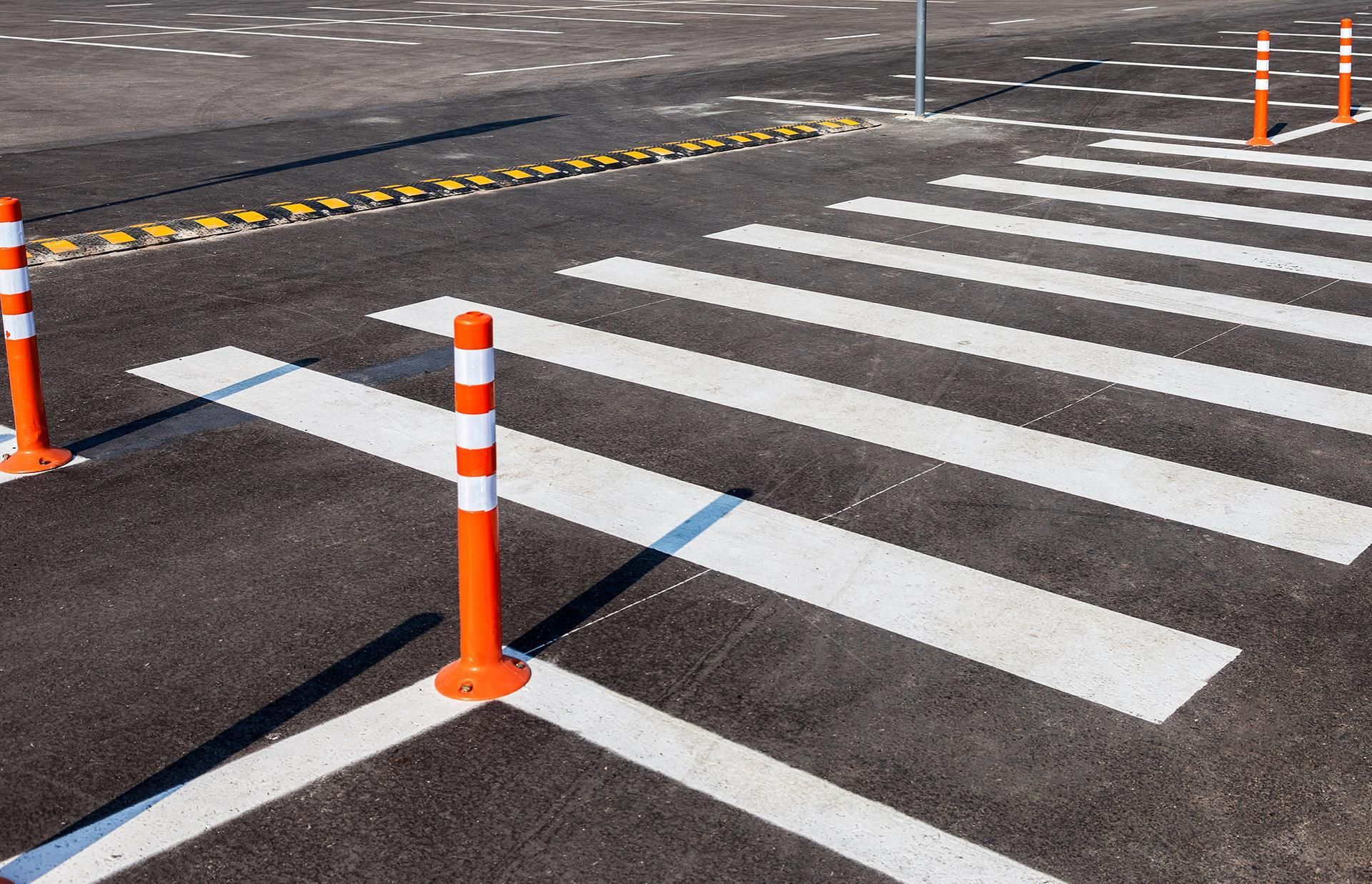 Crosswalk on asphalt with orange bollards.