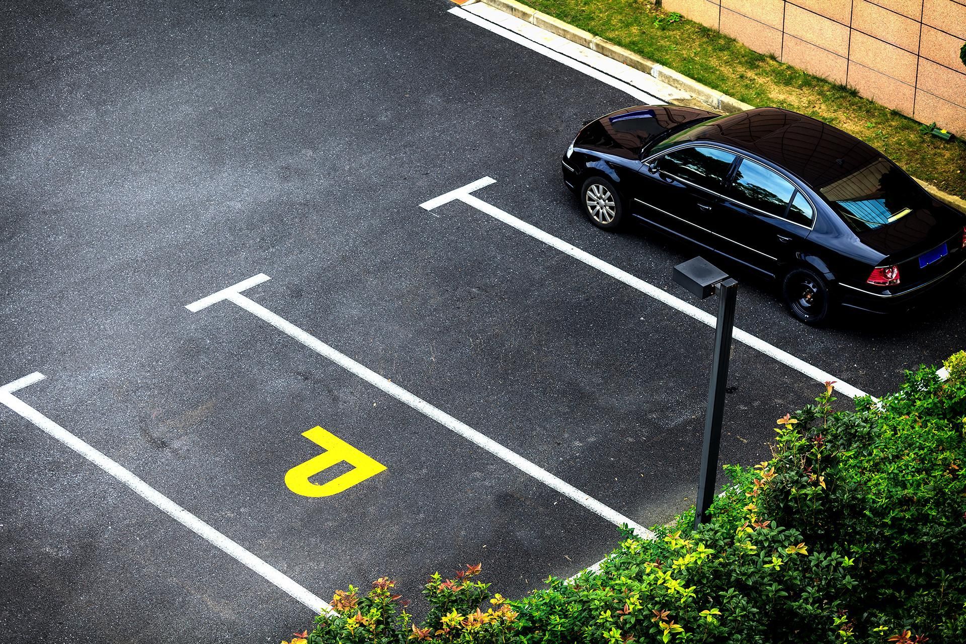 Black car parked in an asphalt parking space marked with white lines and a yellow 