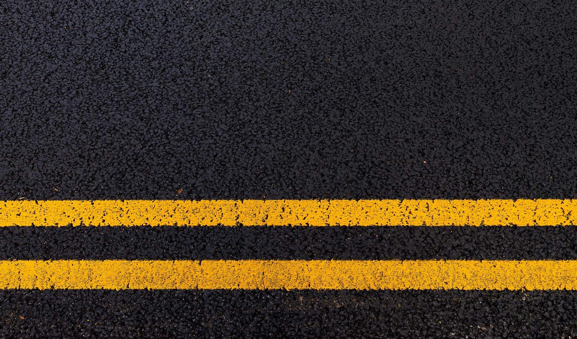 Black asphalt road with two parallel yellow lines.