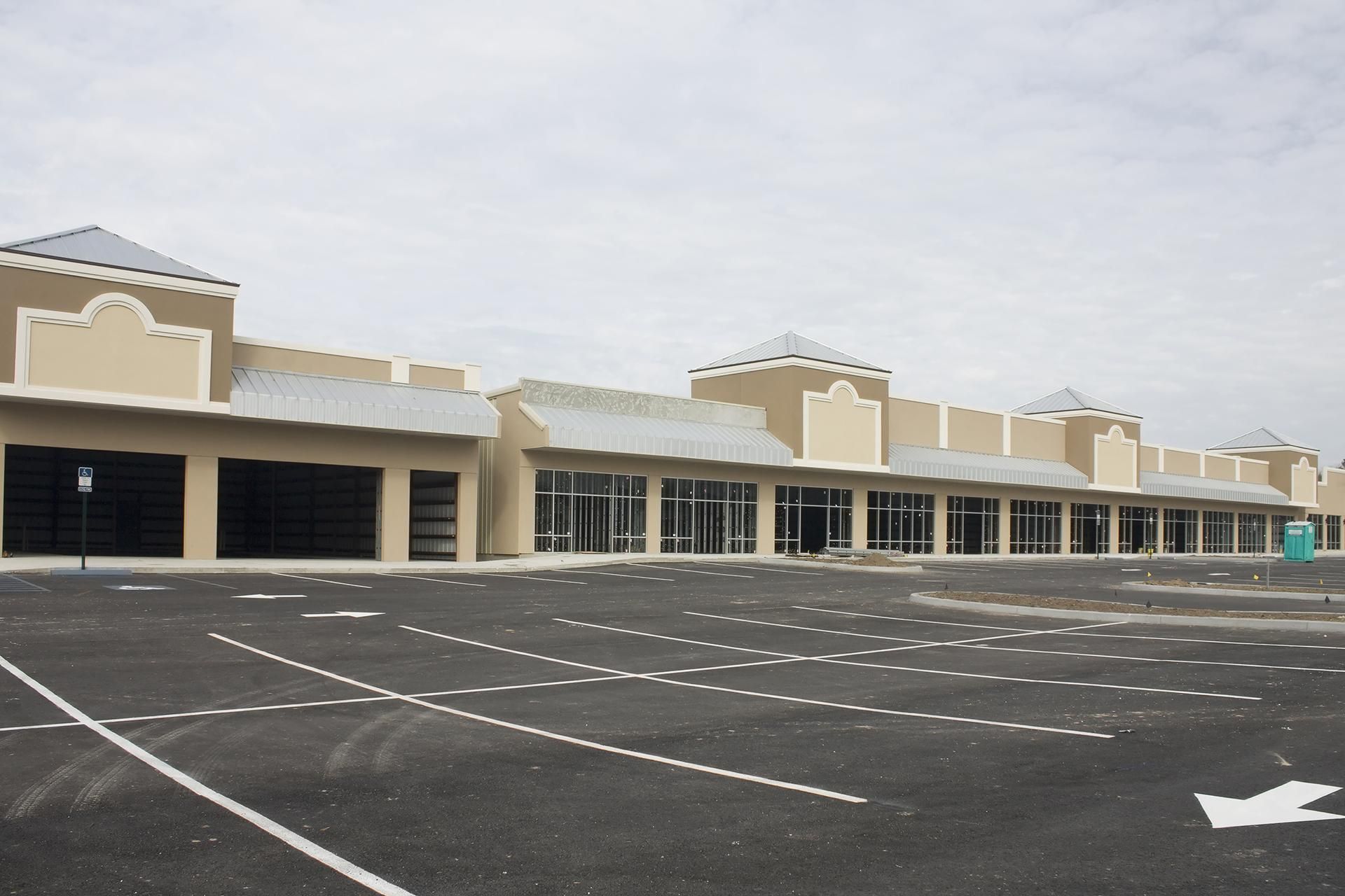 Empty strip mall with a large, empty parking lot under a cloudy sky.