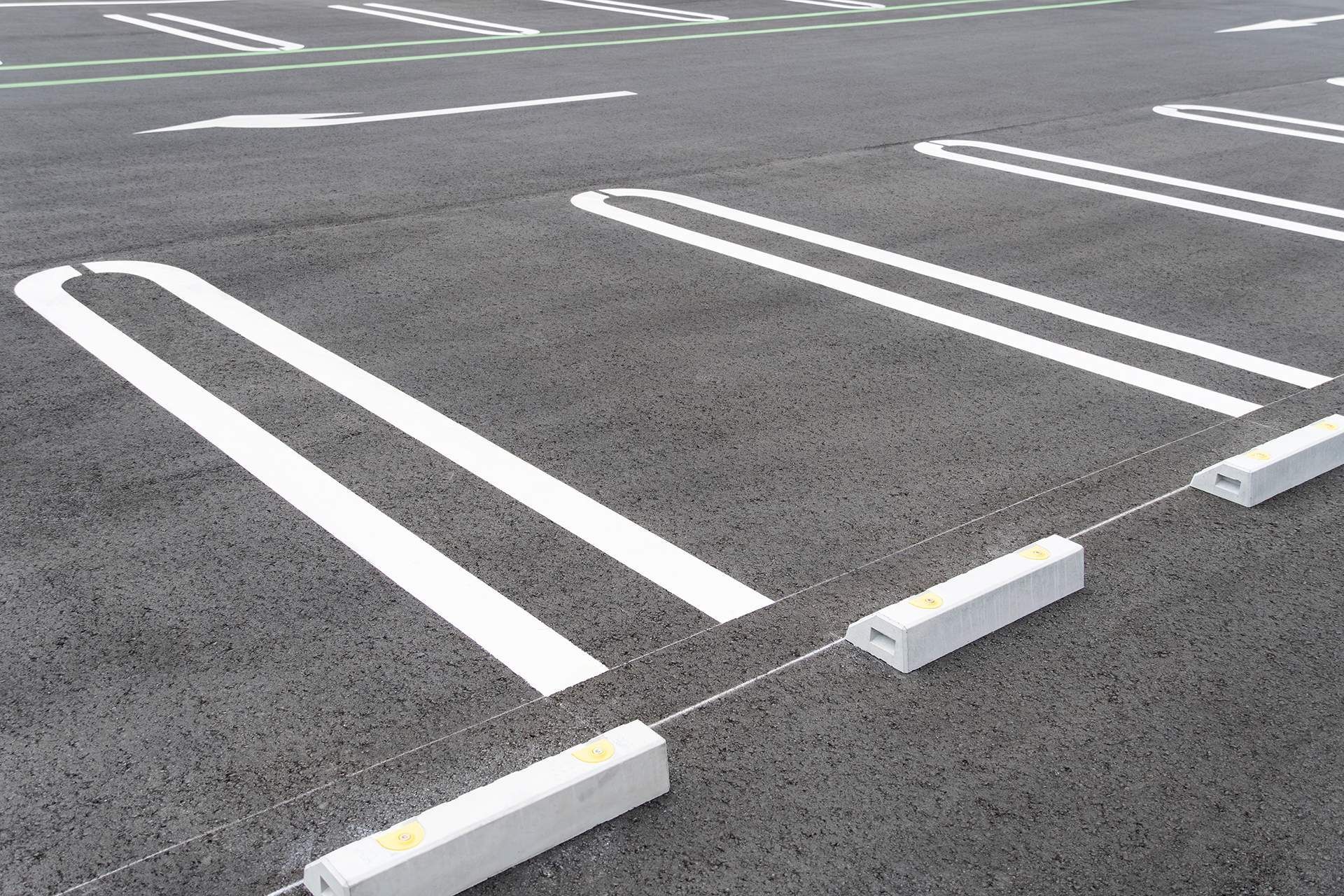 Asphalt parking lot with white painted parking space lines and concrete parking stops.