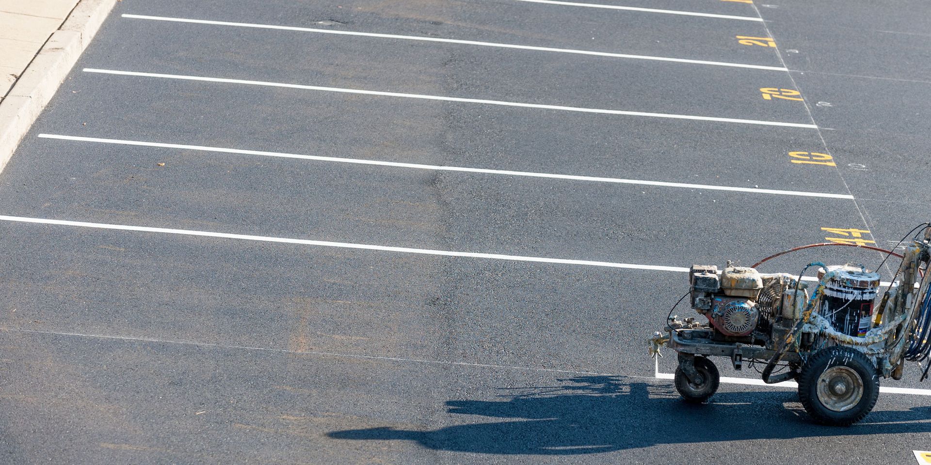 A machine applying white paint to asphalt to create parking lines.