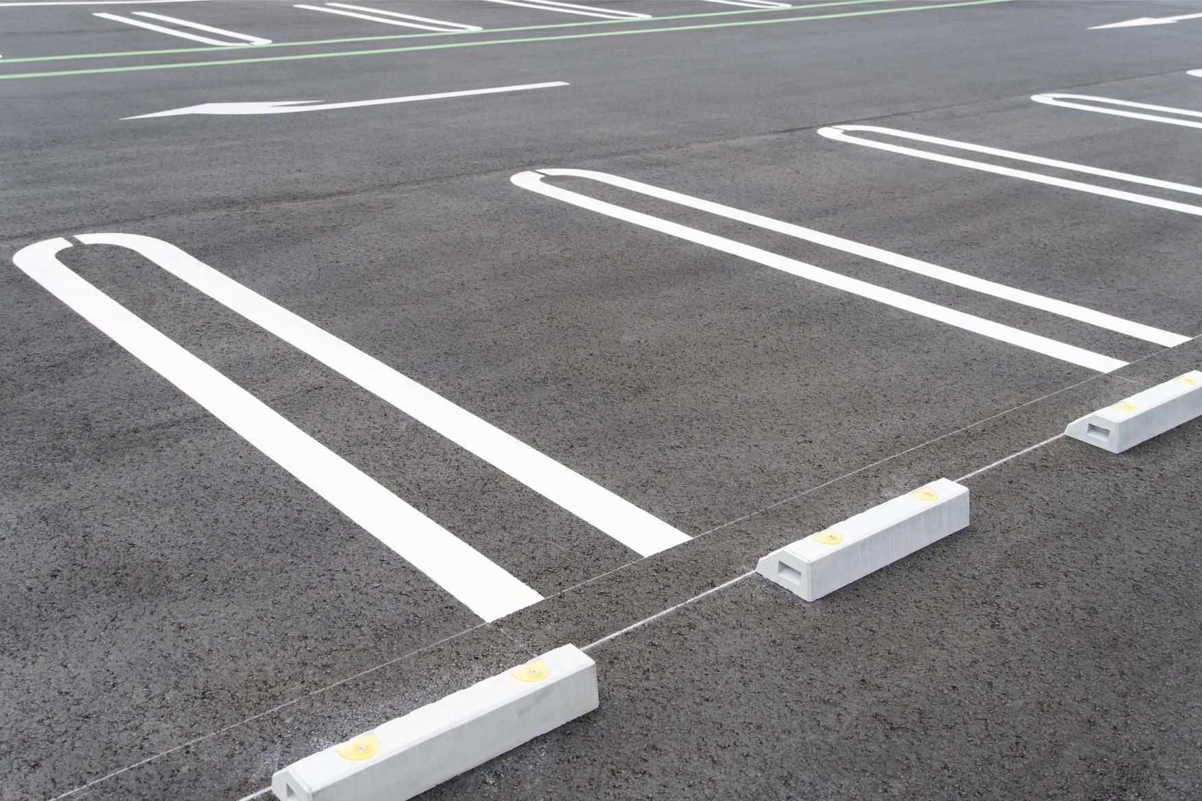 An asphalt parking lot with white painted stall lines and concrete wheel stops.