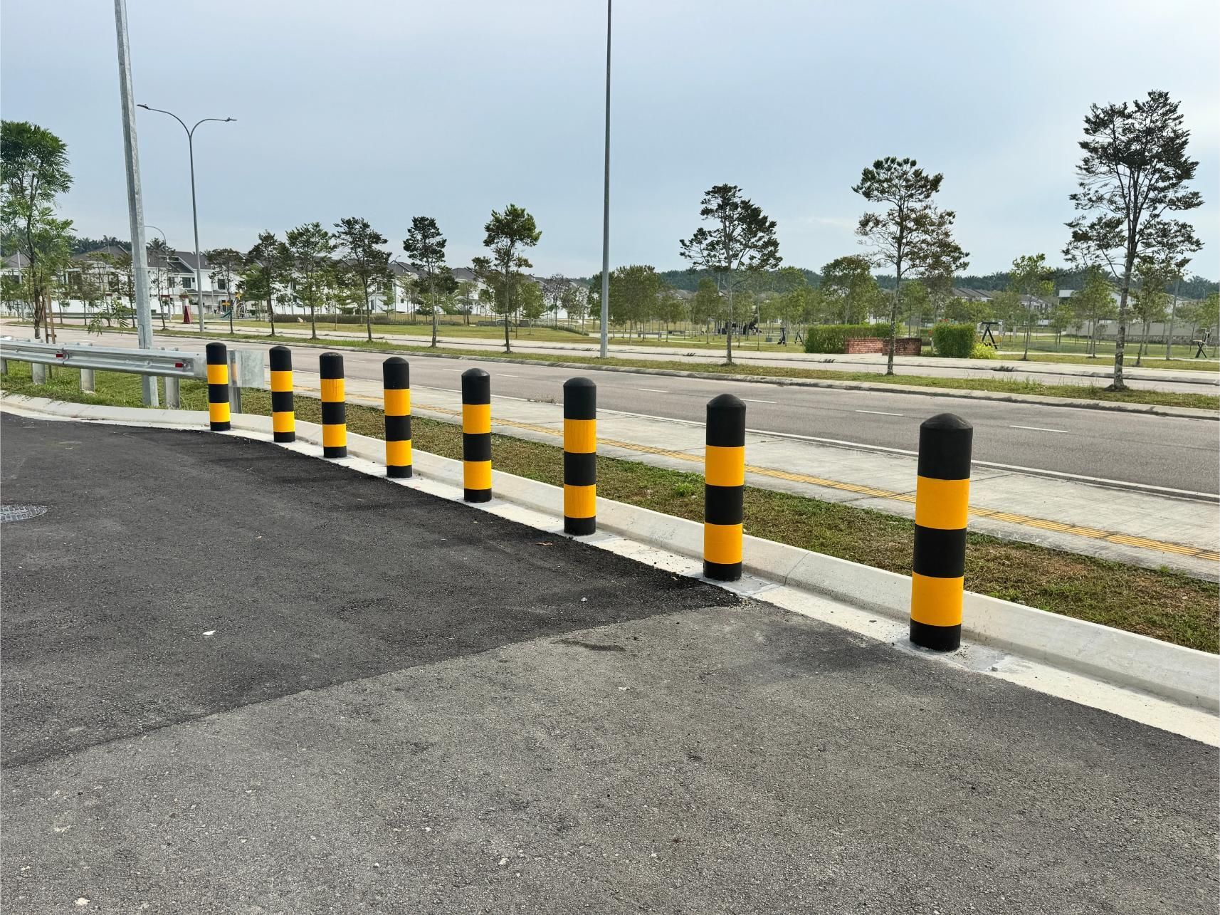 A row of black and yellow bollards standing along the edge of a paved road in a residential area.