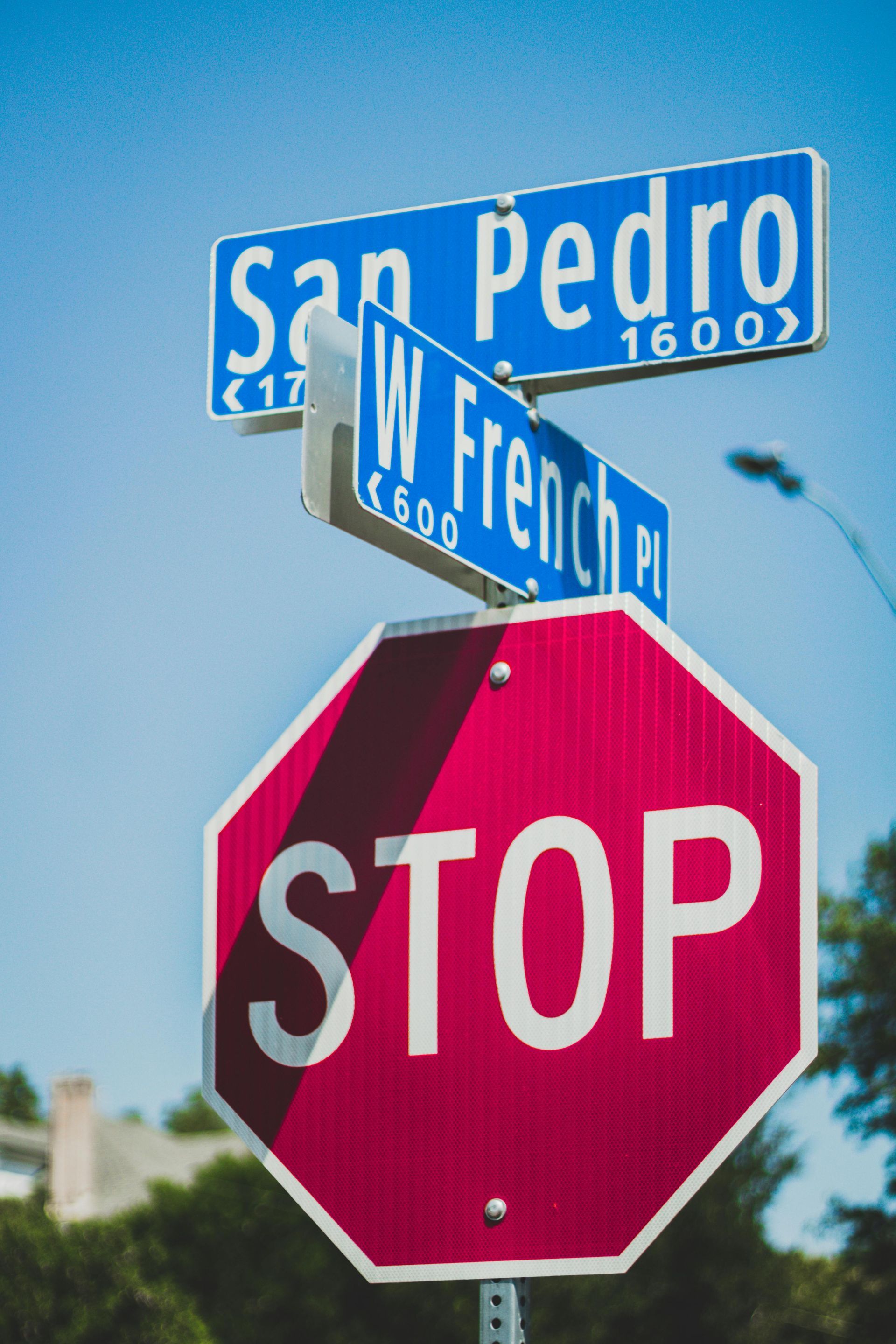 Street signs for San Pedro and W. French Place with a red STOP sign against a blue sky.