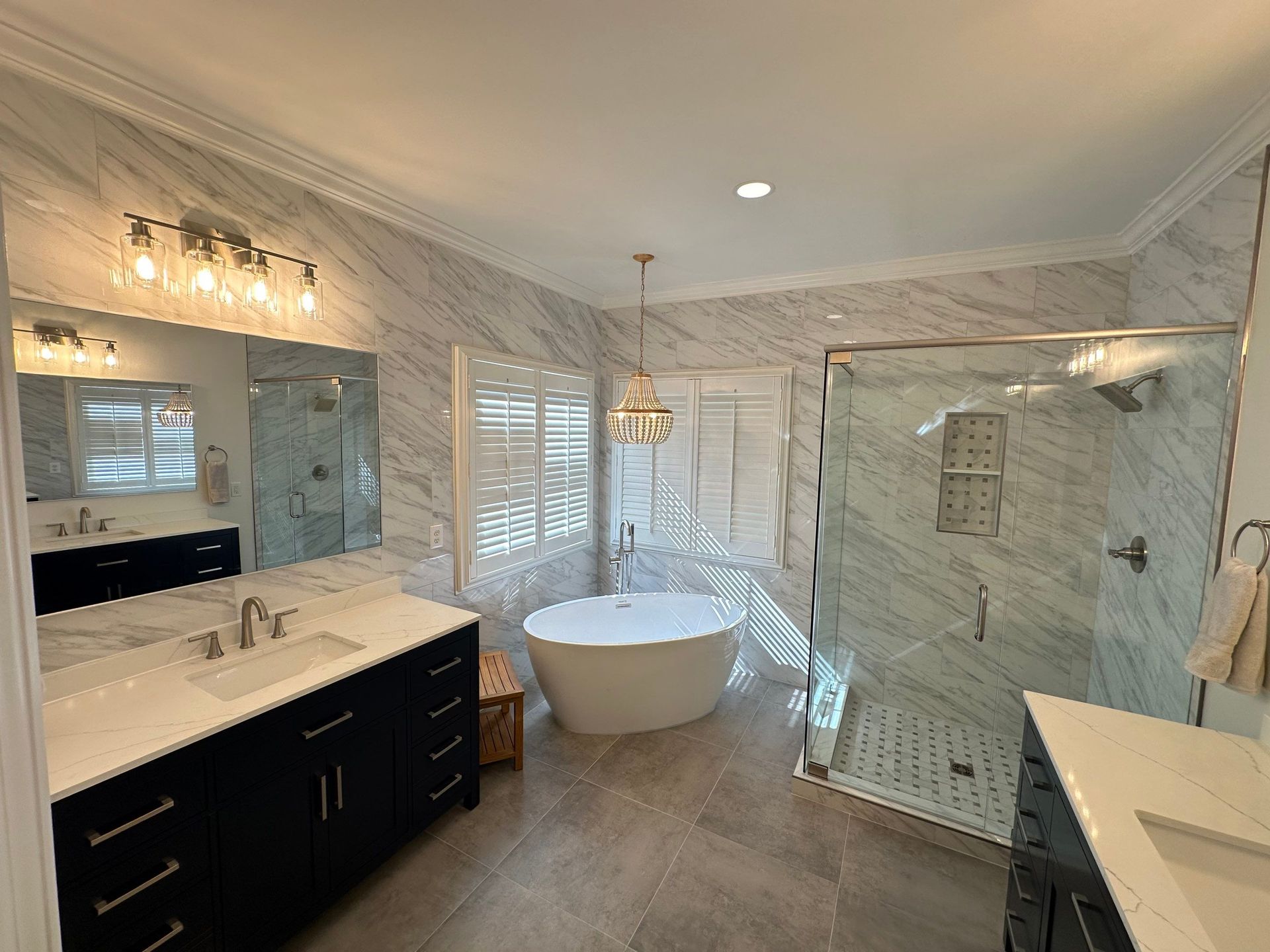 Bright modern bathroom with freestanding tub, glass shower, double vanity, and marble-like finishes